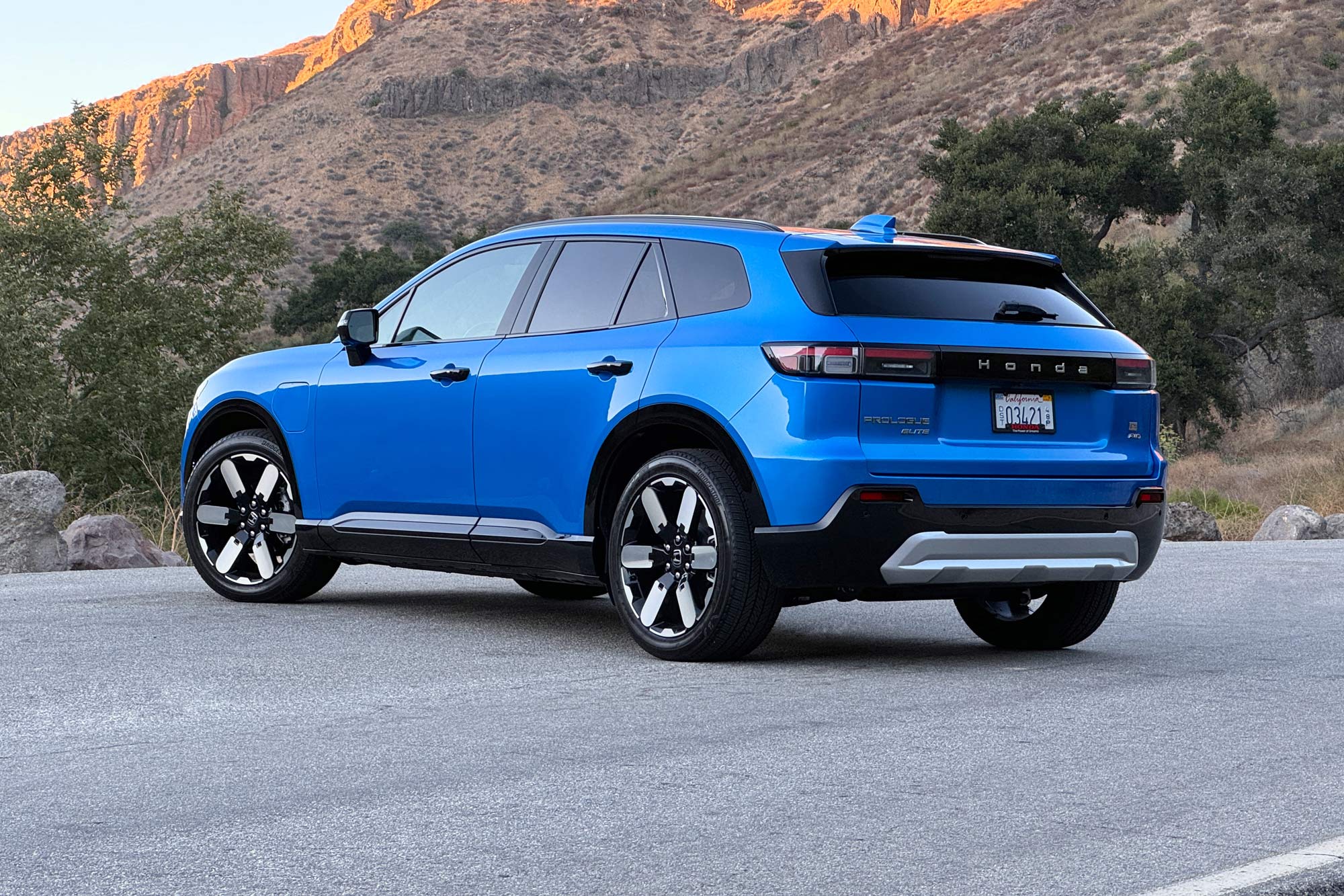 2024 Honda Prologue Elite in Pacific Blue with a brush-covered hill and rocky bluff in the background.