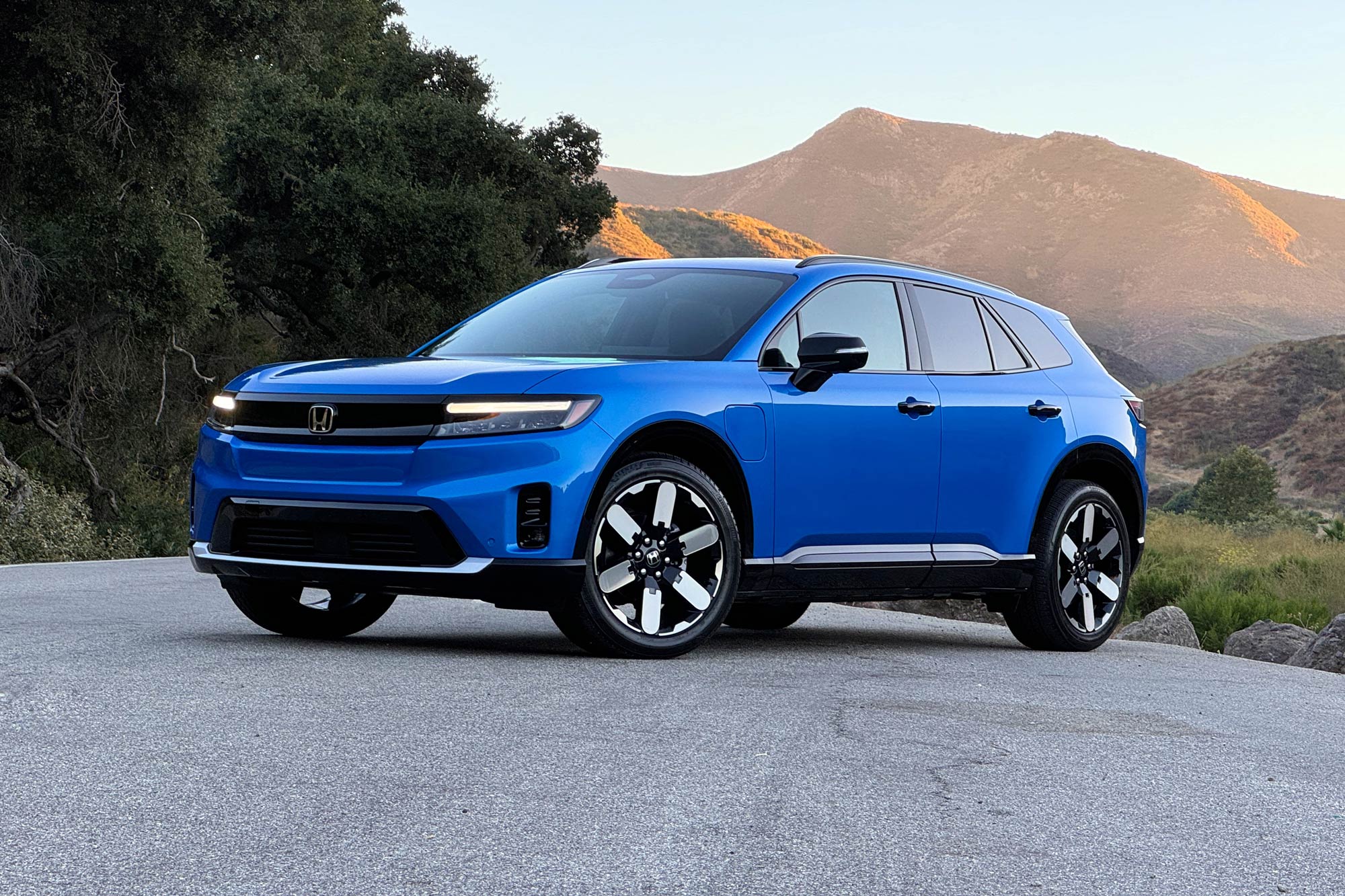 2024 Honda Prologue Elite in Pacific Blue with trees and mountains in the background.