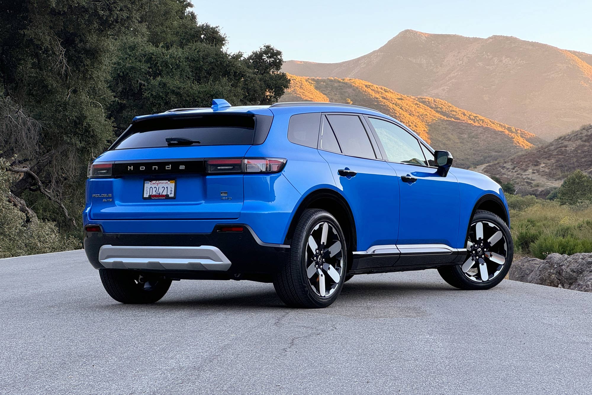 2024 Honda Prologue Elite in Pacific Blue with trees and mountains in the background.