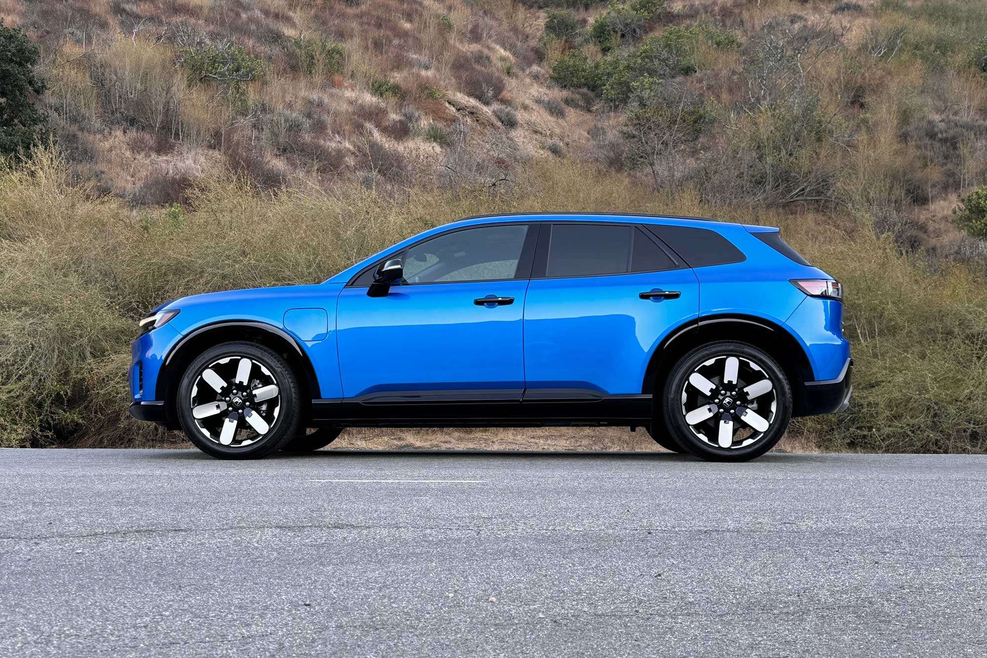 2024 Honda Prologue Elite in Pacific Blue with a brush-covered hill in the background.