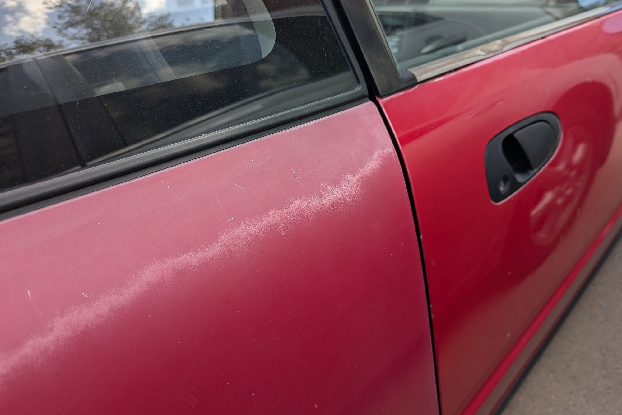 Two doors on a red car, one with faded paint