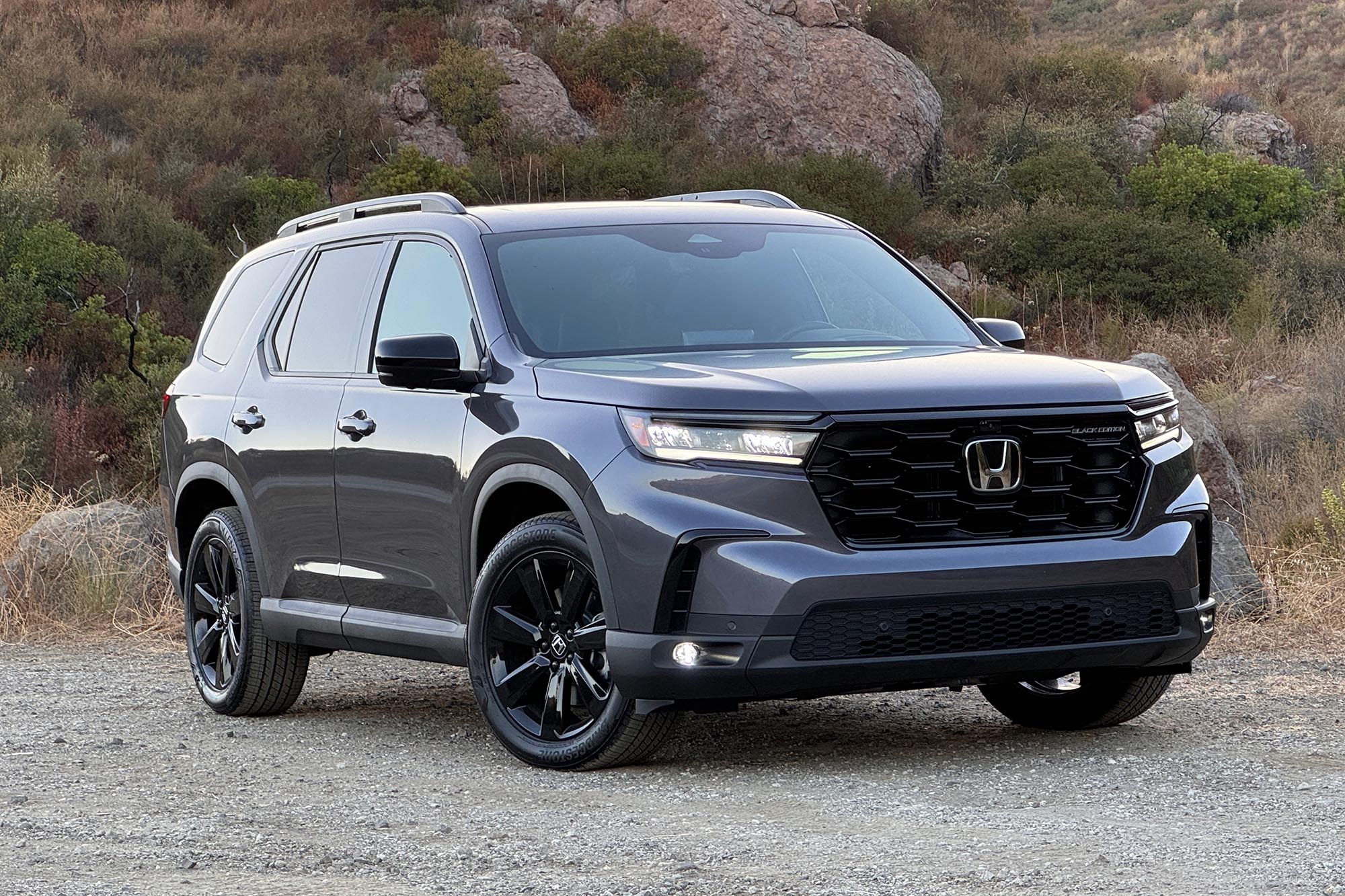 2025 Honda Pilot Black Edition in Modern Steel with boulders and a brush-covered hill in the background.