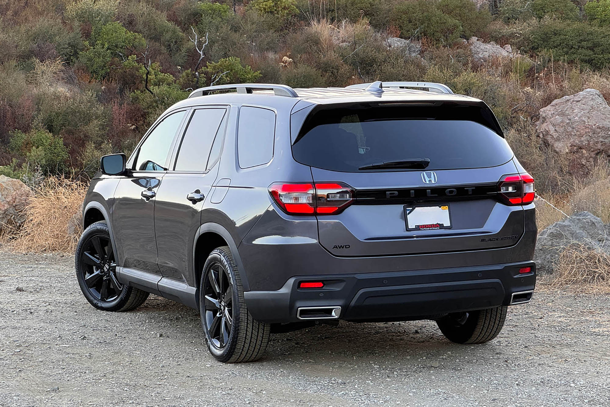 2025 Honda Pilot Black Edition in Modern Steel with boulders and a brush-covered hill in the background.