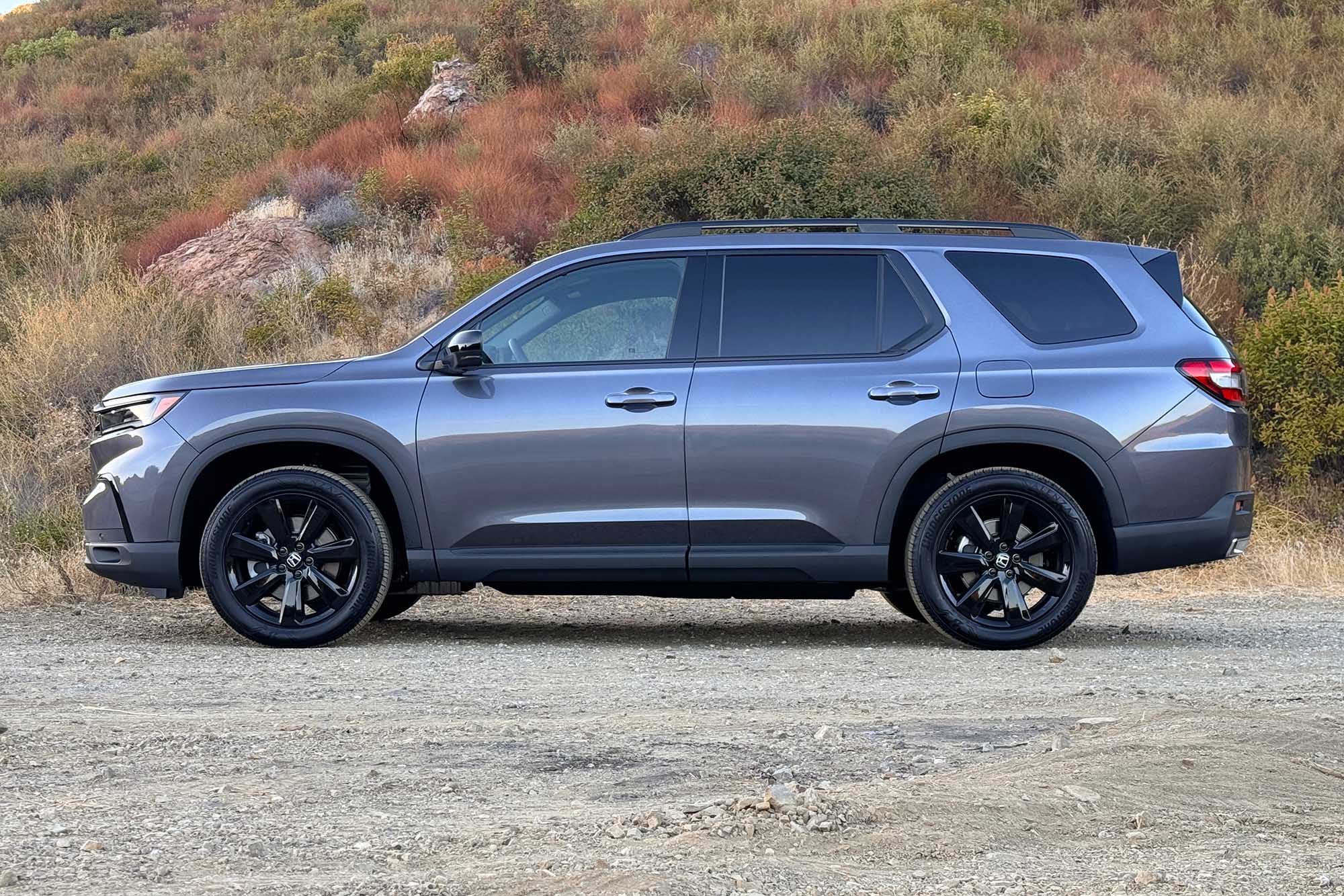 2025 Honda Pilot Black Edition in Modern Steel with a brush-covered hill in the background.