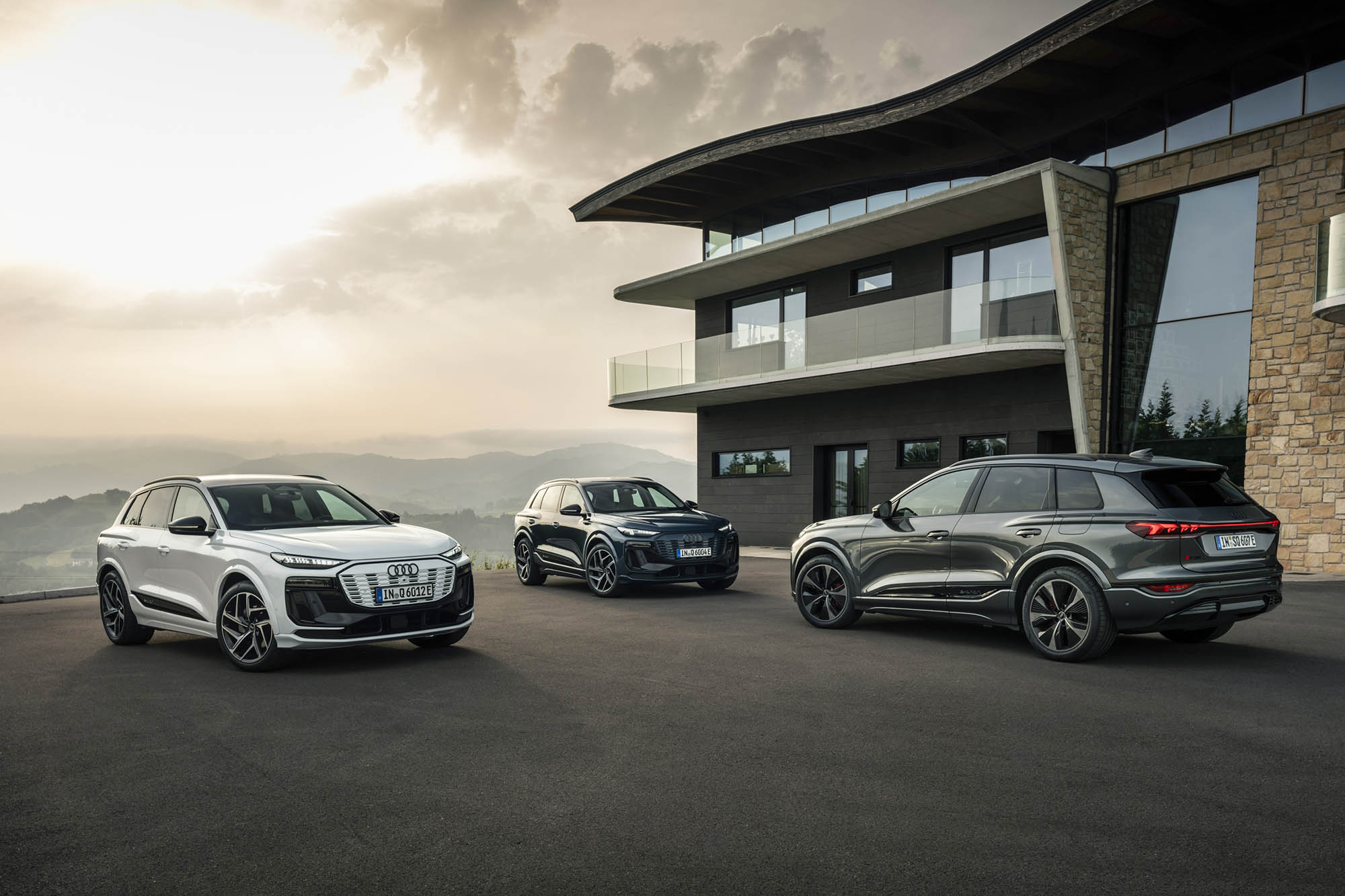 Three 2025 Audi Q6 e-trons parked in front of a modern building