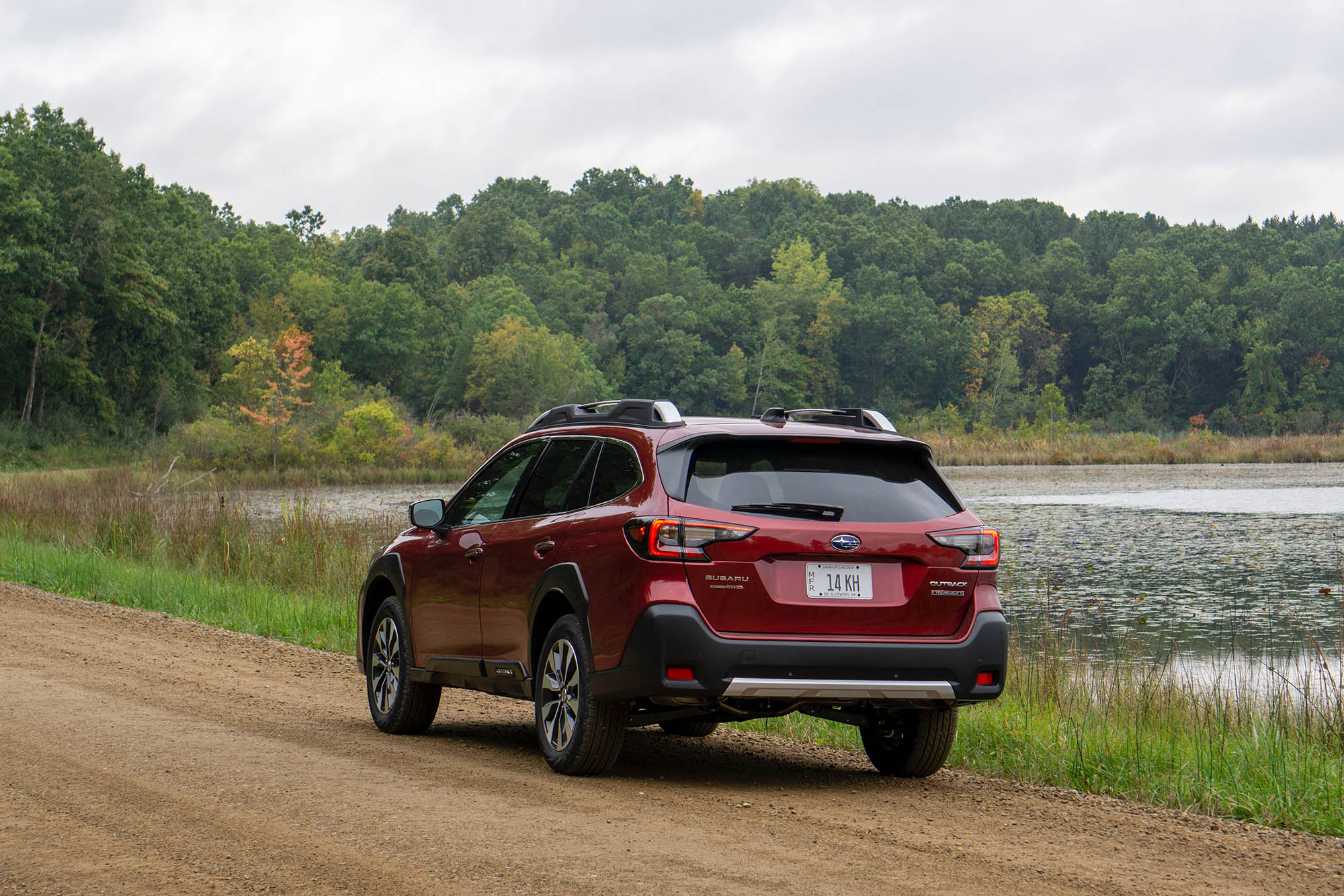 2025 Subaru Outback Touring XT in Crimson Red Pearl, rear view with trees and a pond in the background