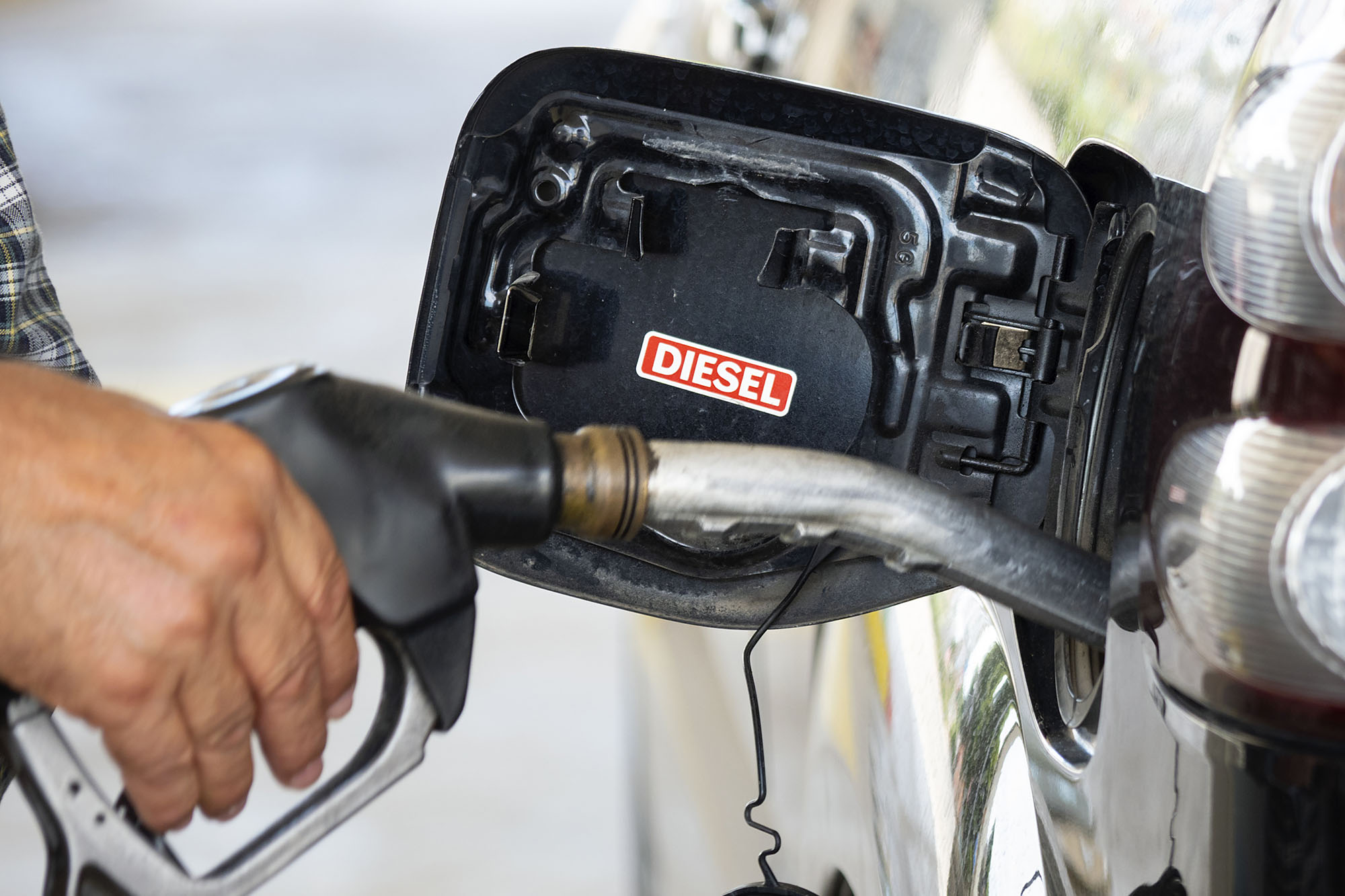 A person's hand holds a diesel fuel pump to refill a vehicle's tank