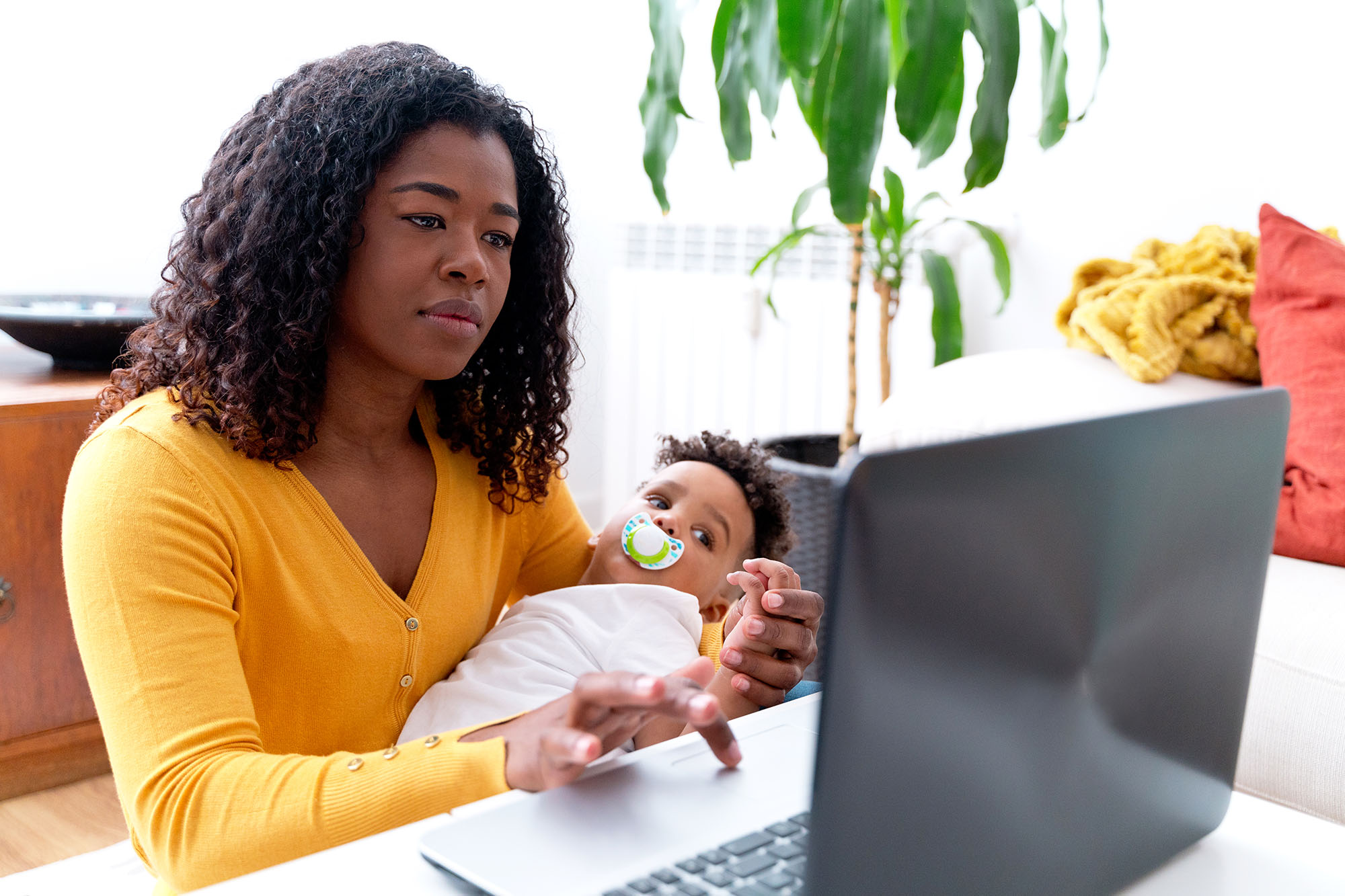 Person holding a baby looks at a laptop computer screen in a home setting