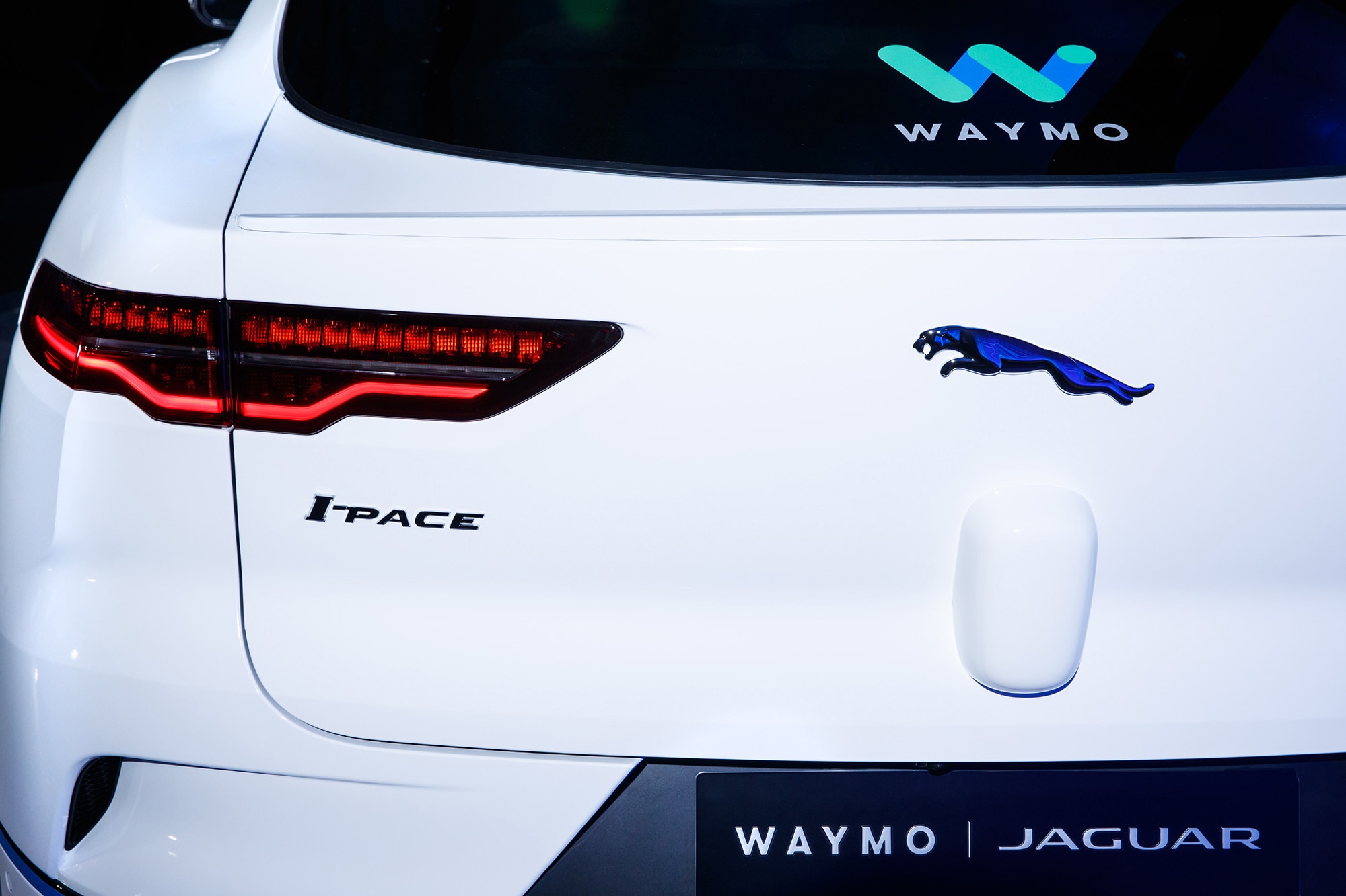 Rear detail view of a white Jaguar I-Pace in Waymo One robo-taxi livery.