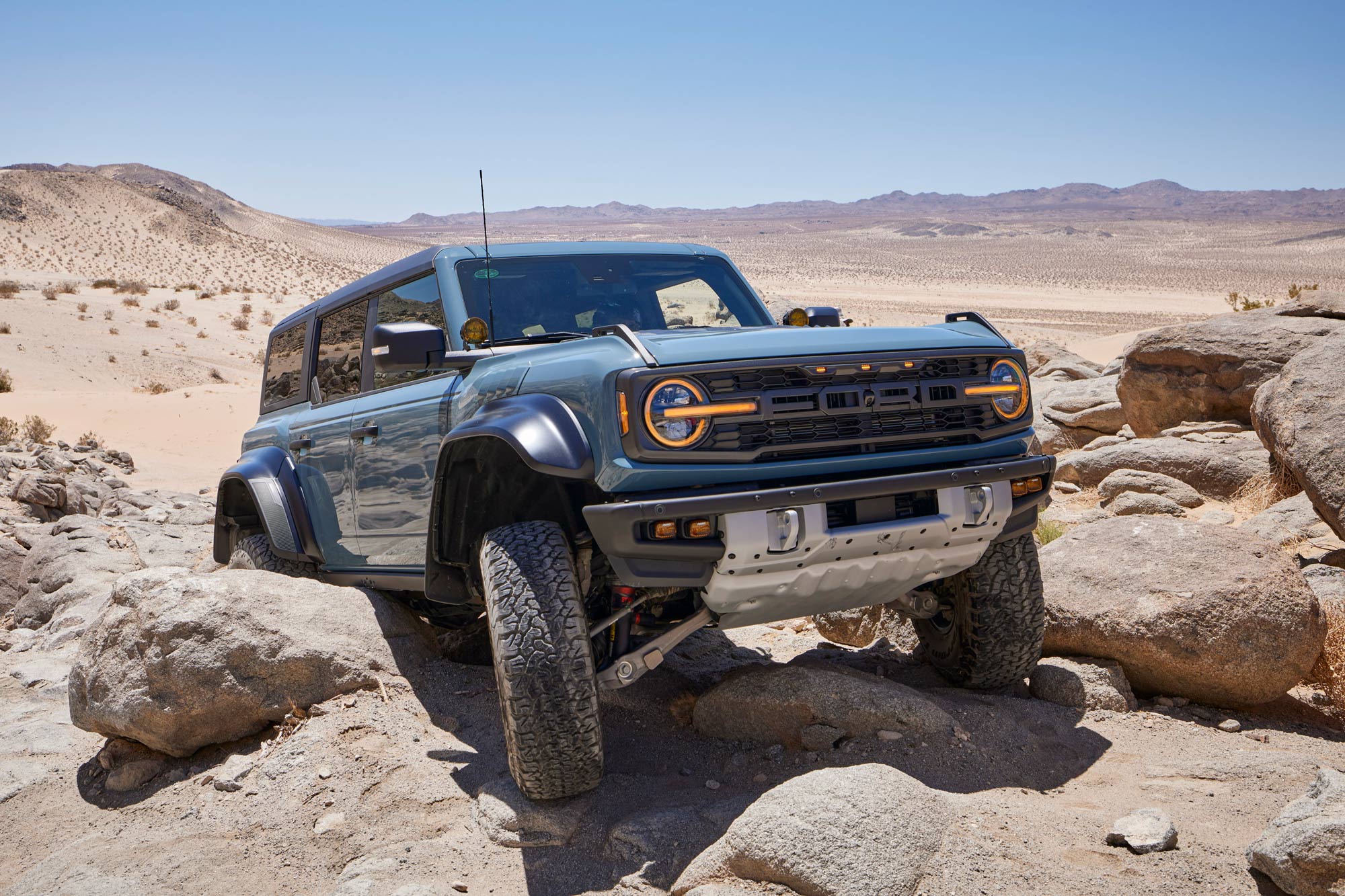 A blue 2024 Ford Bronco Raptor climbing rocks