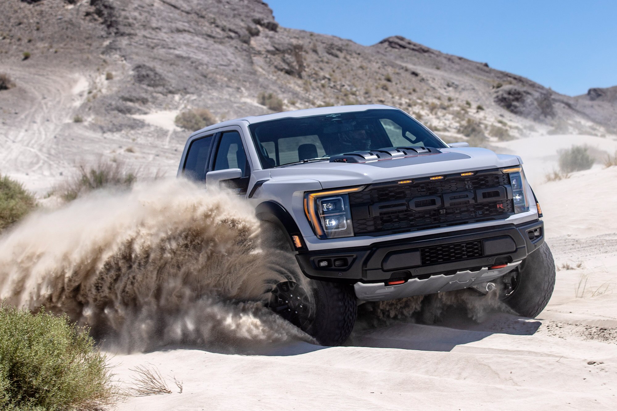 A gray Ford F-150 Raptor running through sand