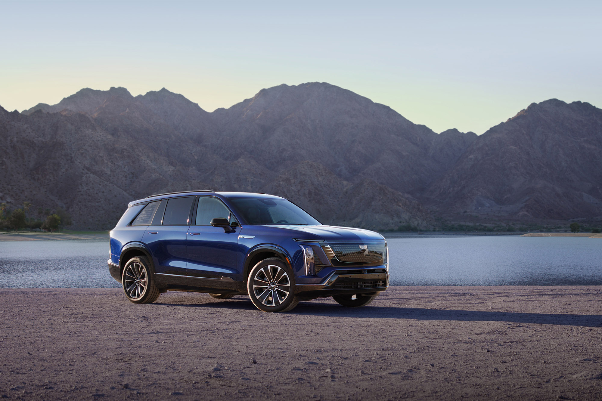 2026 Cadillac Vistiq in Opulent Blue Metallic parked in front of a lake and mountains.