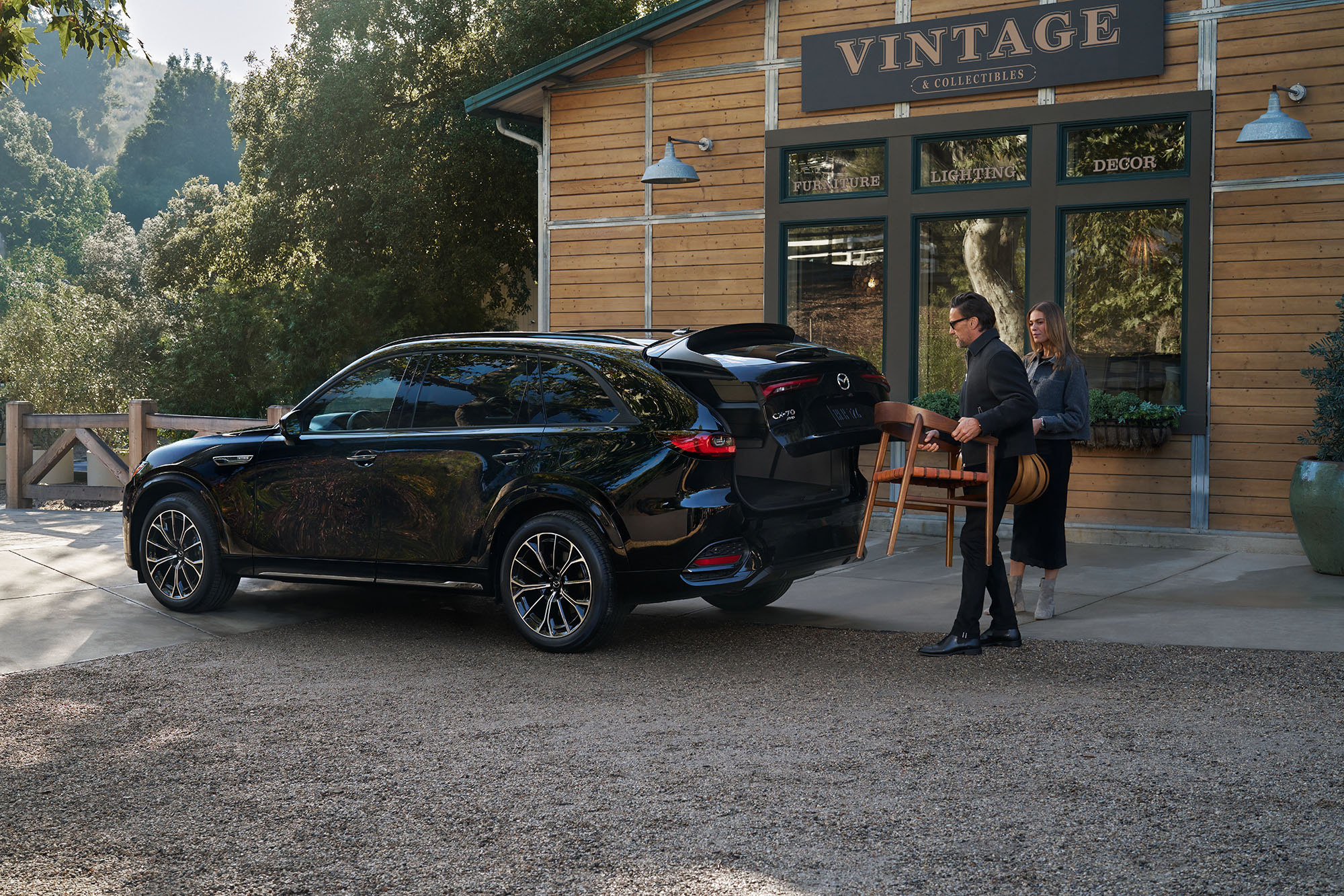 Two people load a chair into the back of a black 2025 Mazda CX-70