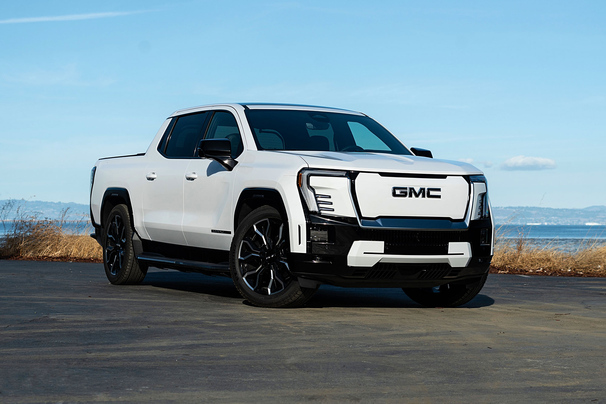 2025 GMC Sierra EV Denali in Summit White with the ocean and distant mountains in the background.