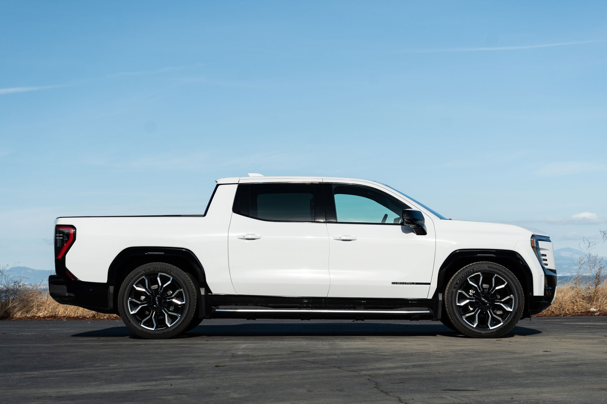 2025 GMC Sierra EV Denali in Summit White with blue sky and distant mountains in the background.