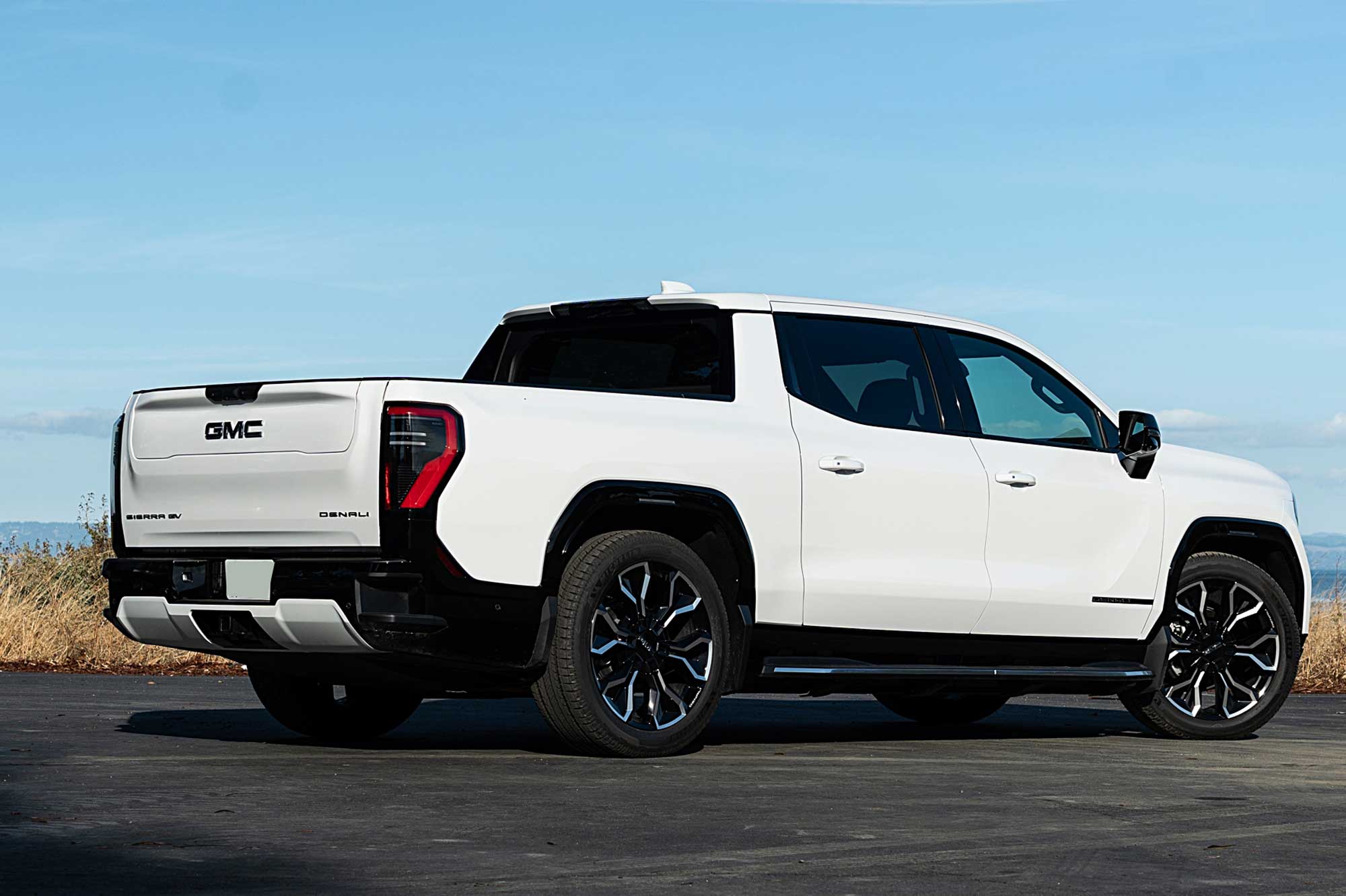 2025 GMC Sierra EV Denali in Summit White with the ocean and distant mountains in the background.