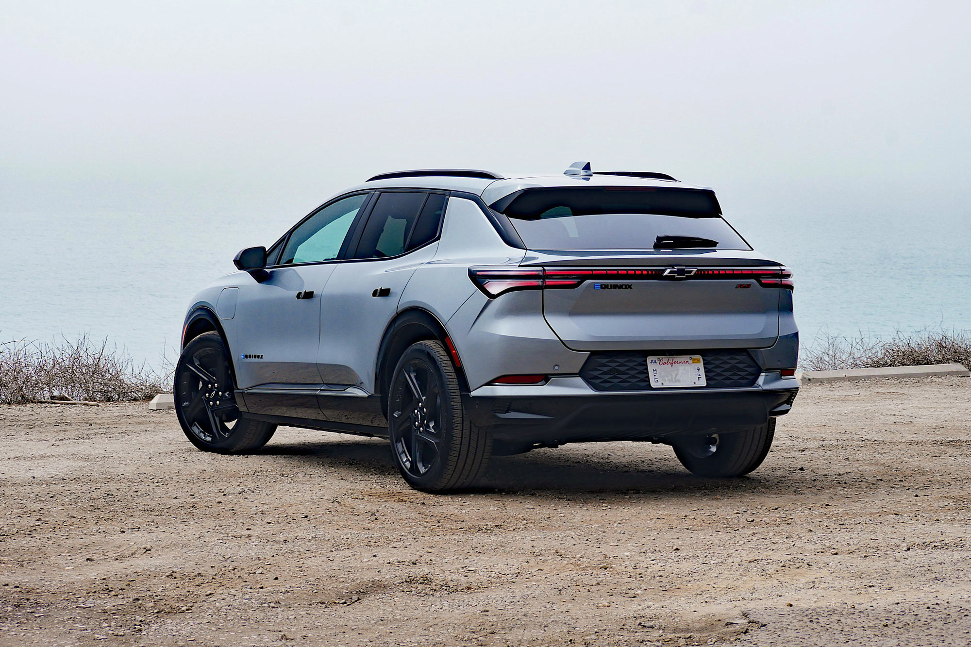 Rear quarter 2024 Chevrolet Equinox EV 3RS in Sterling Gray with the foggy Pacific Ocean in the background