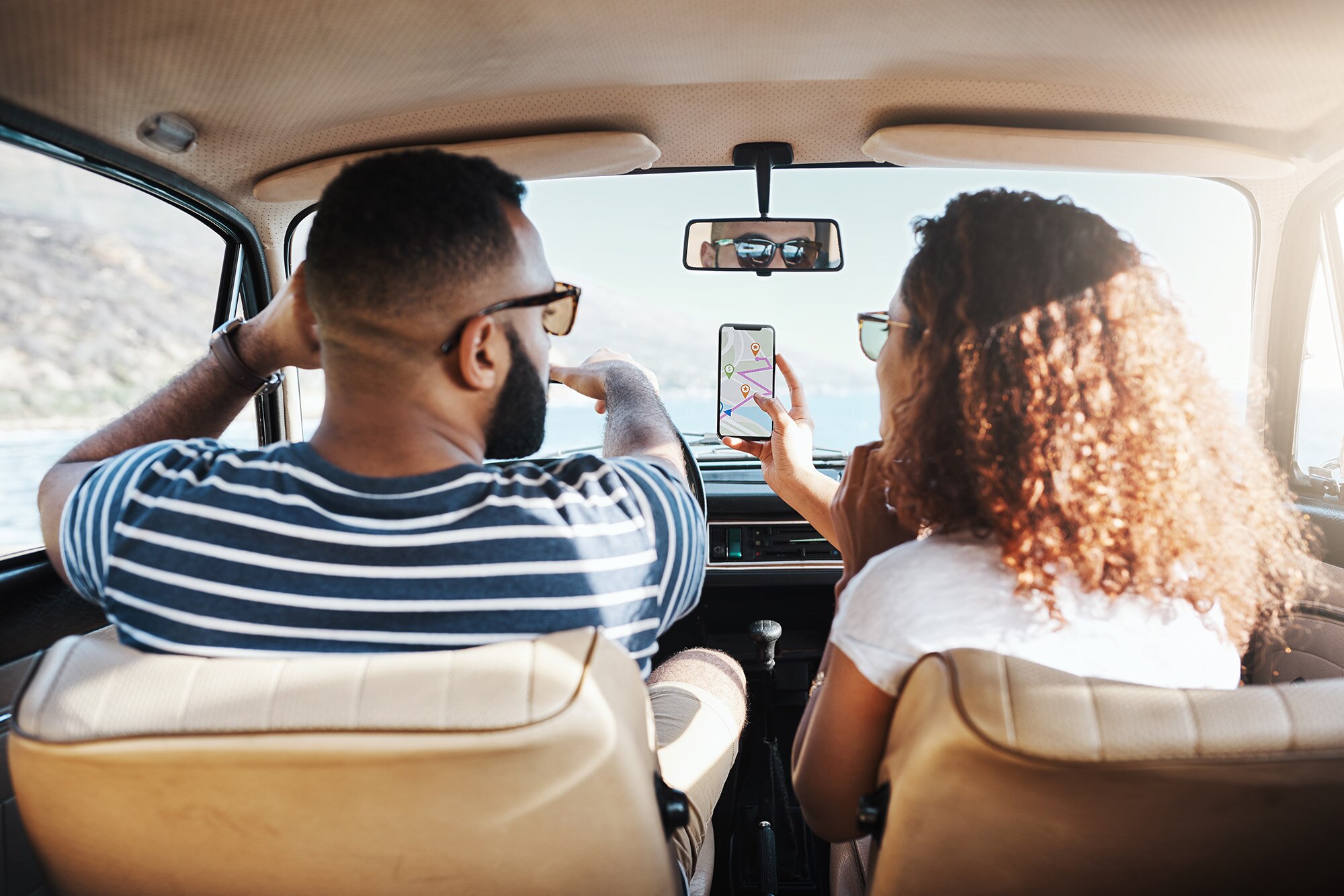 A driver and front-seat passenger in a vehicle look at a smartphone with a map on the screen