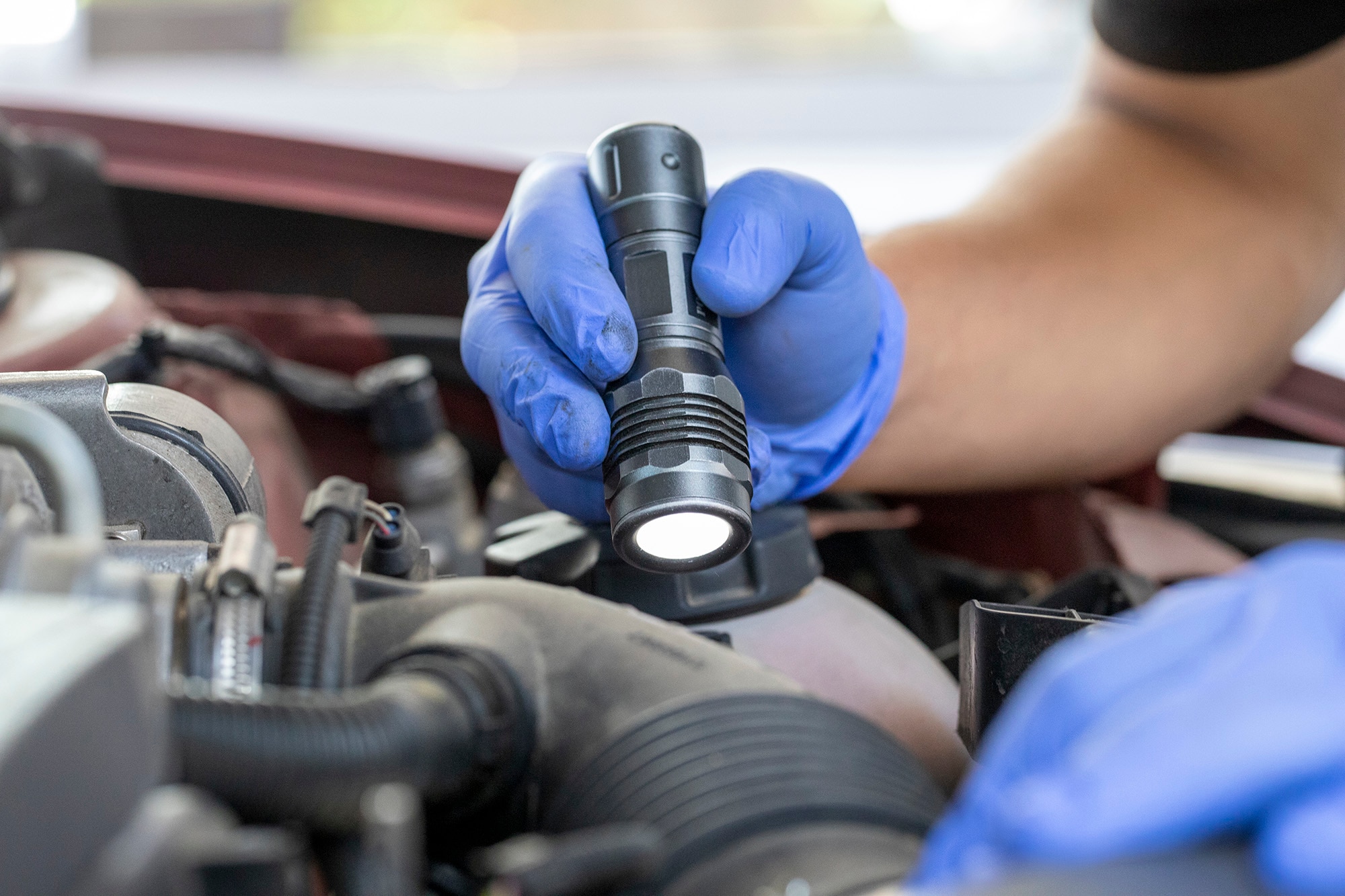 Person's hand holds a small flashlight over the engine bay of a vehicle