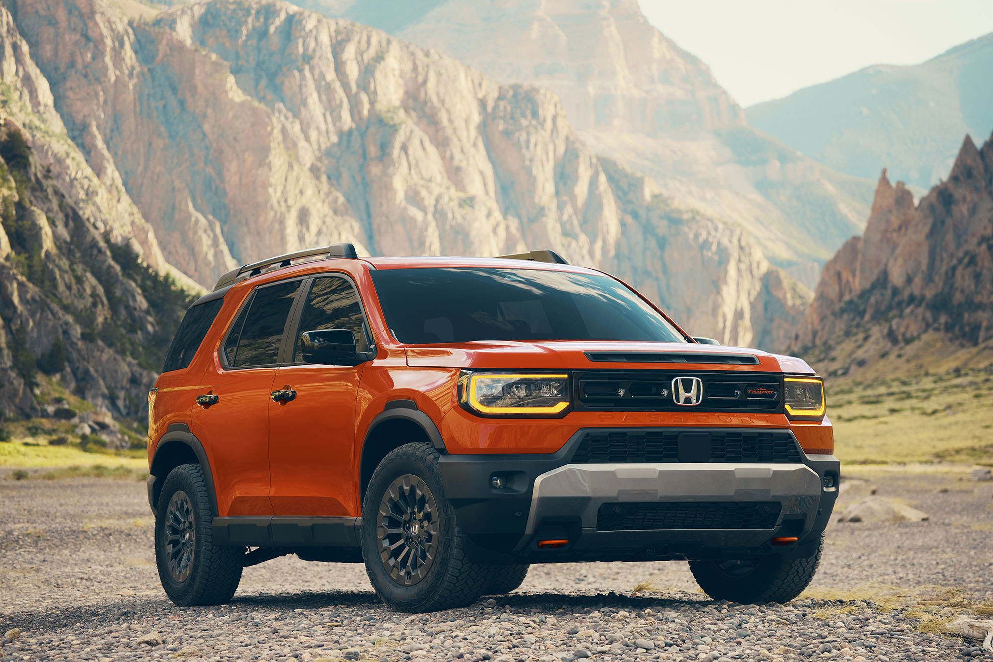 A front-right view of an orange 2026 Honda Passport TrailSport in front of mountains