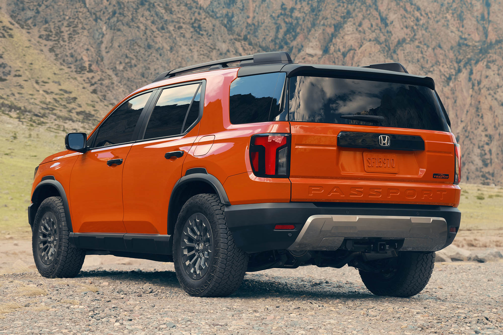 A rear-left view of an orange 2026 Honda Passport TrailSport in front of mountains