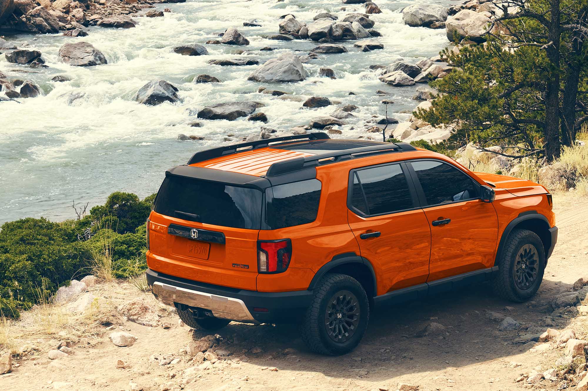 An orange 2026 Honda Passport TrailSport driving on a trail next to a river