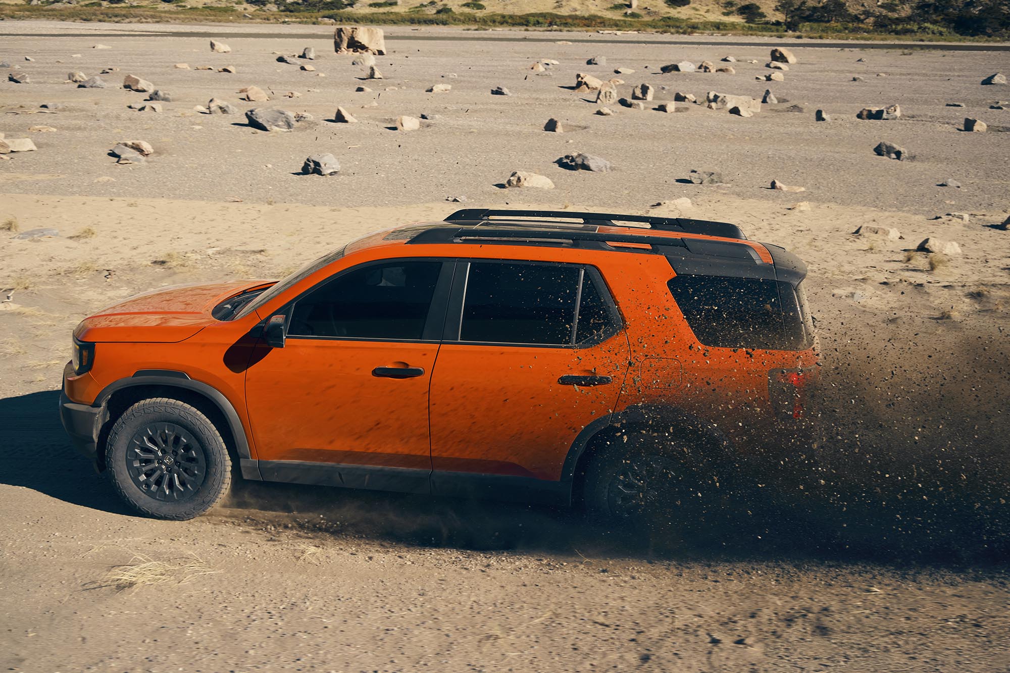 Side view of an orange 2026 Honda Passport TrailSport kicking up dirt