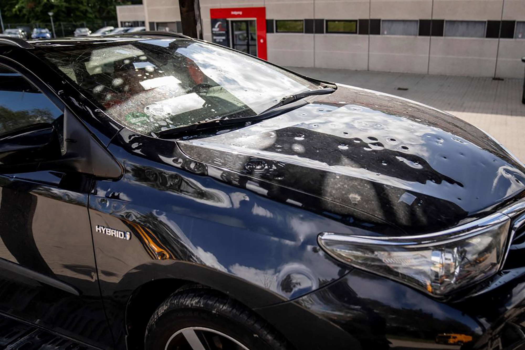 A black car's hood dented from hail damage