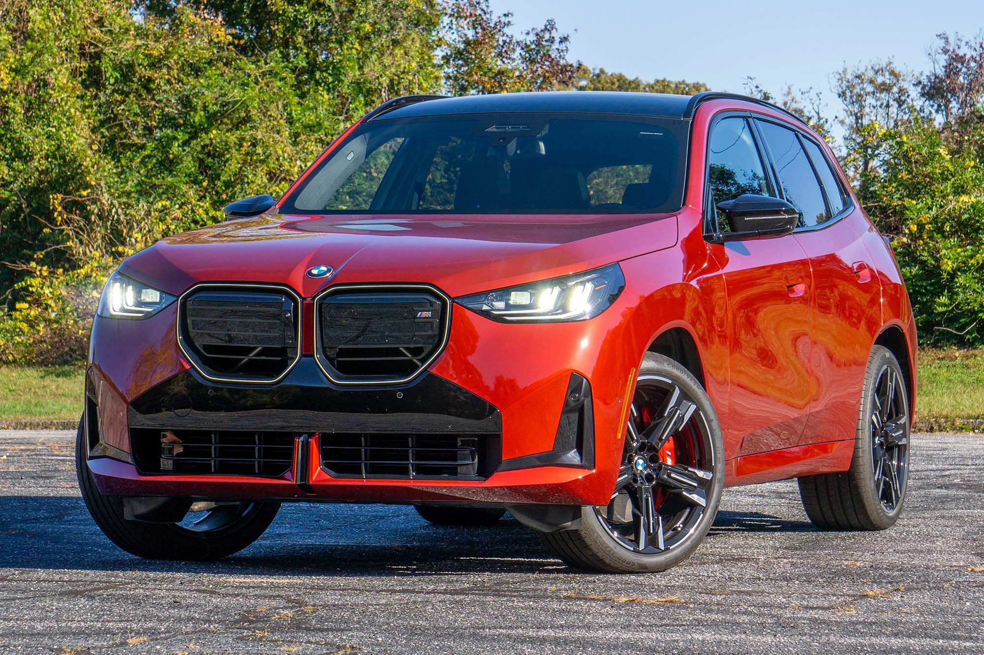 Font left view of a red 2025 BMW X3 in front of trees