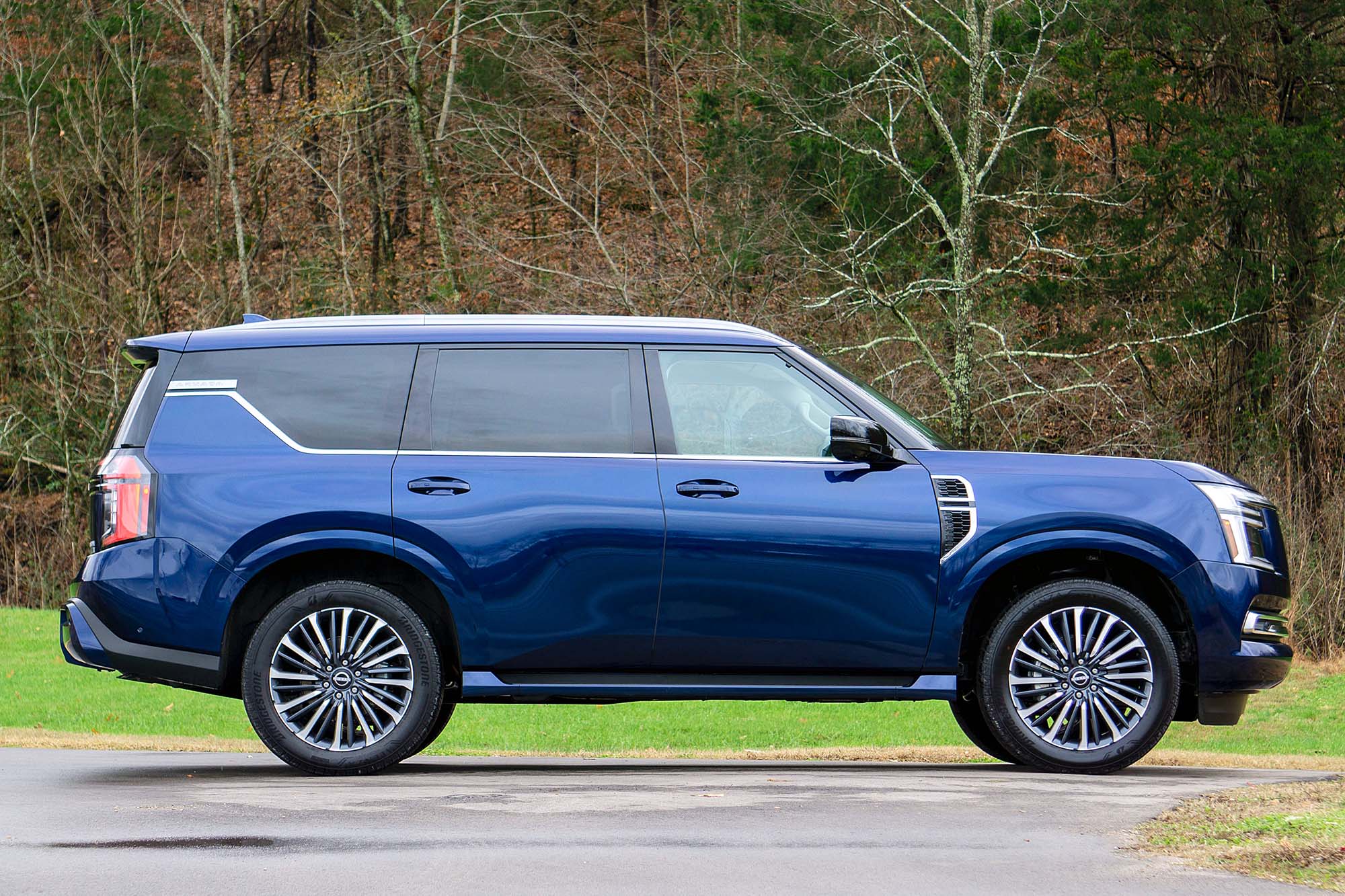 2025 Nissan Armada Platinum Reserve in Ocean Blue Pearl, side view, with grass and a forest in the background.