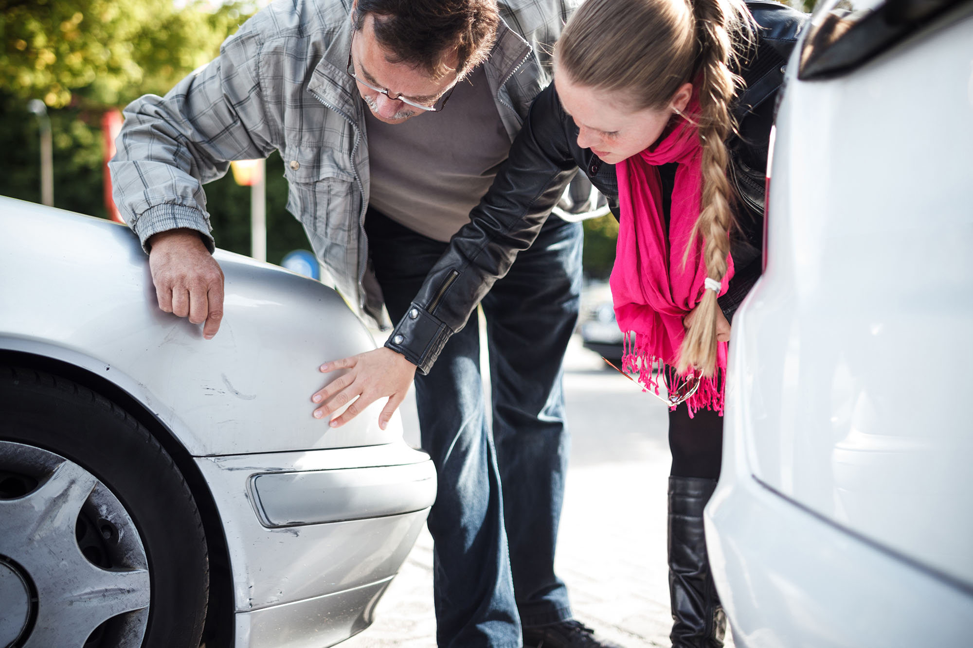 Two people examine marks on a vehicle's silver paint