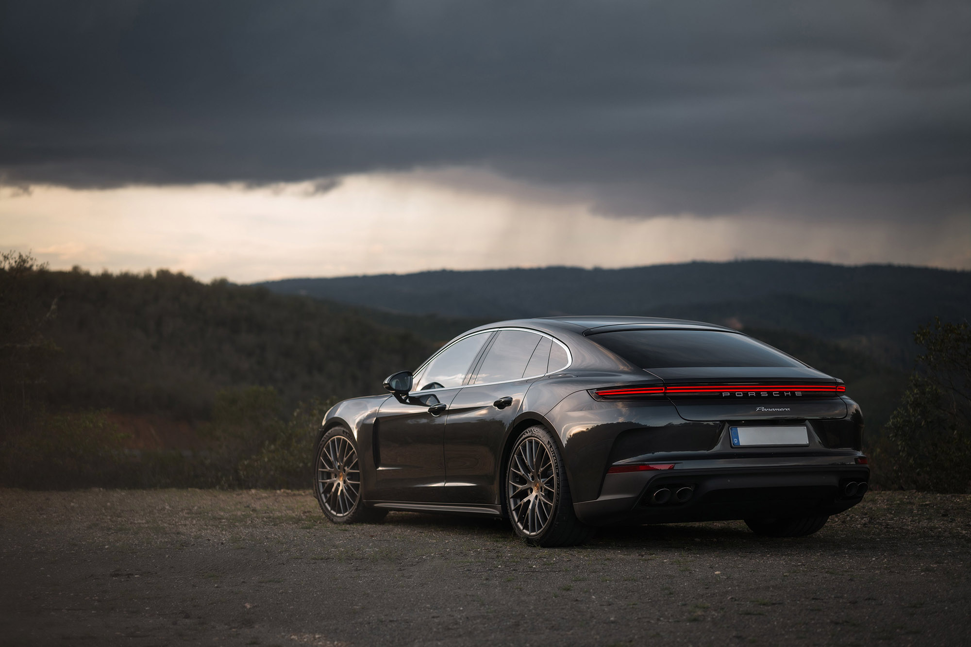 Black Porsche sedan parked overlooking vegetation beneath a cloudy sky