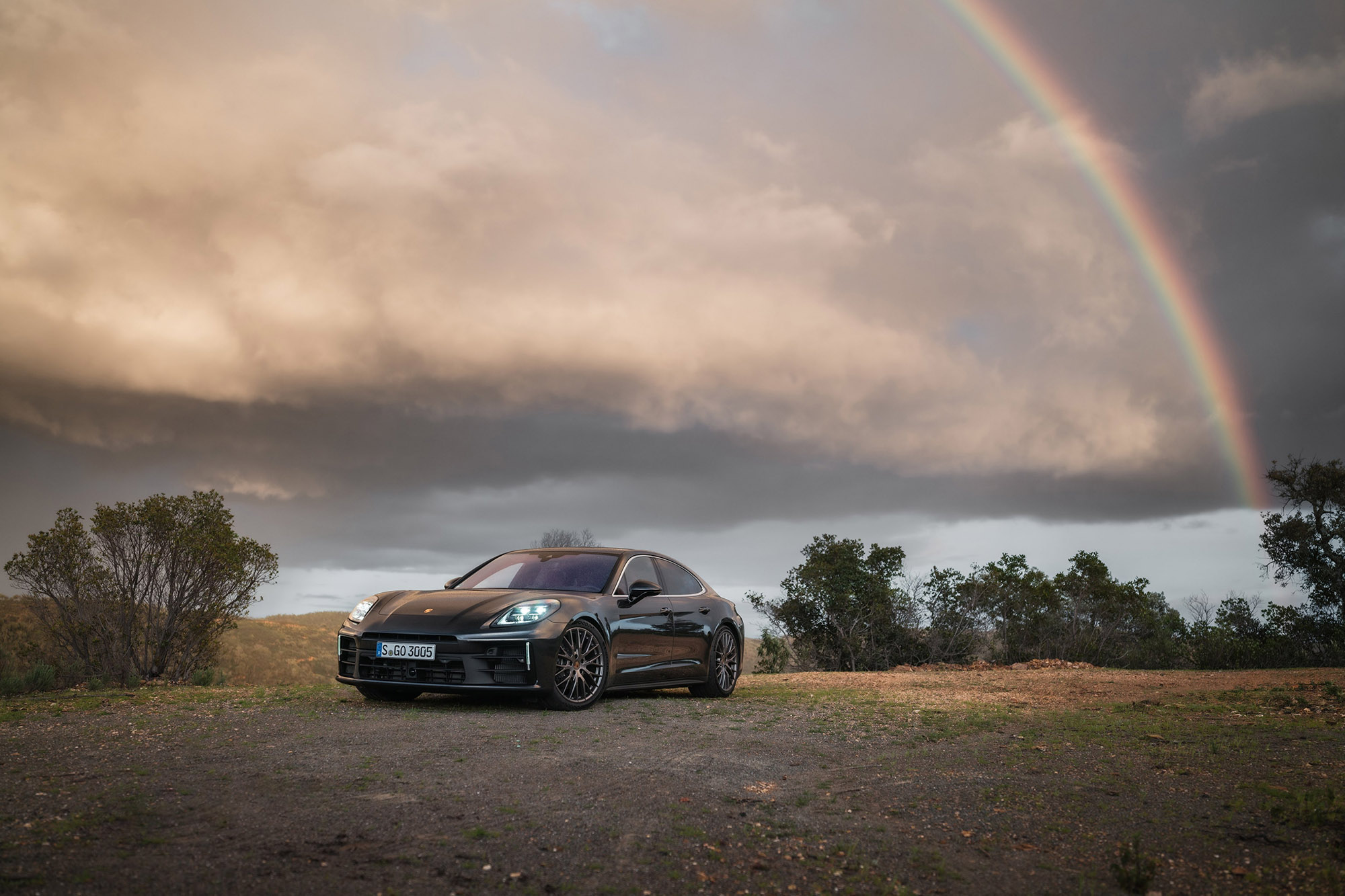 Black Porsche sedan parked beneath a rainbow