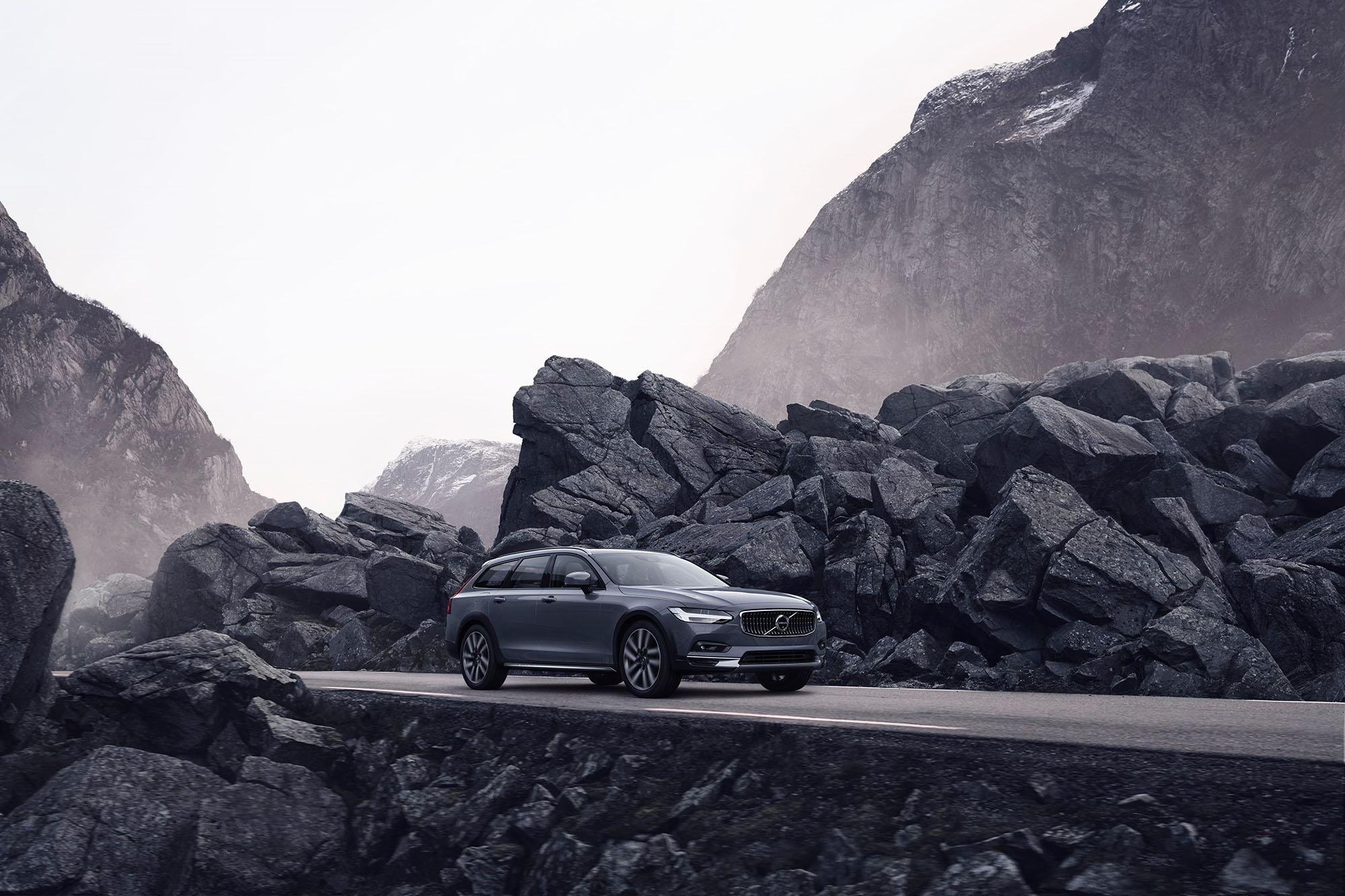 Gray Volvo SUV driving on a road surrounded by black rocks