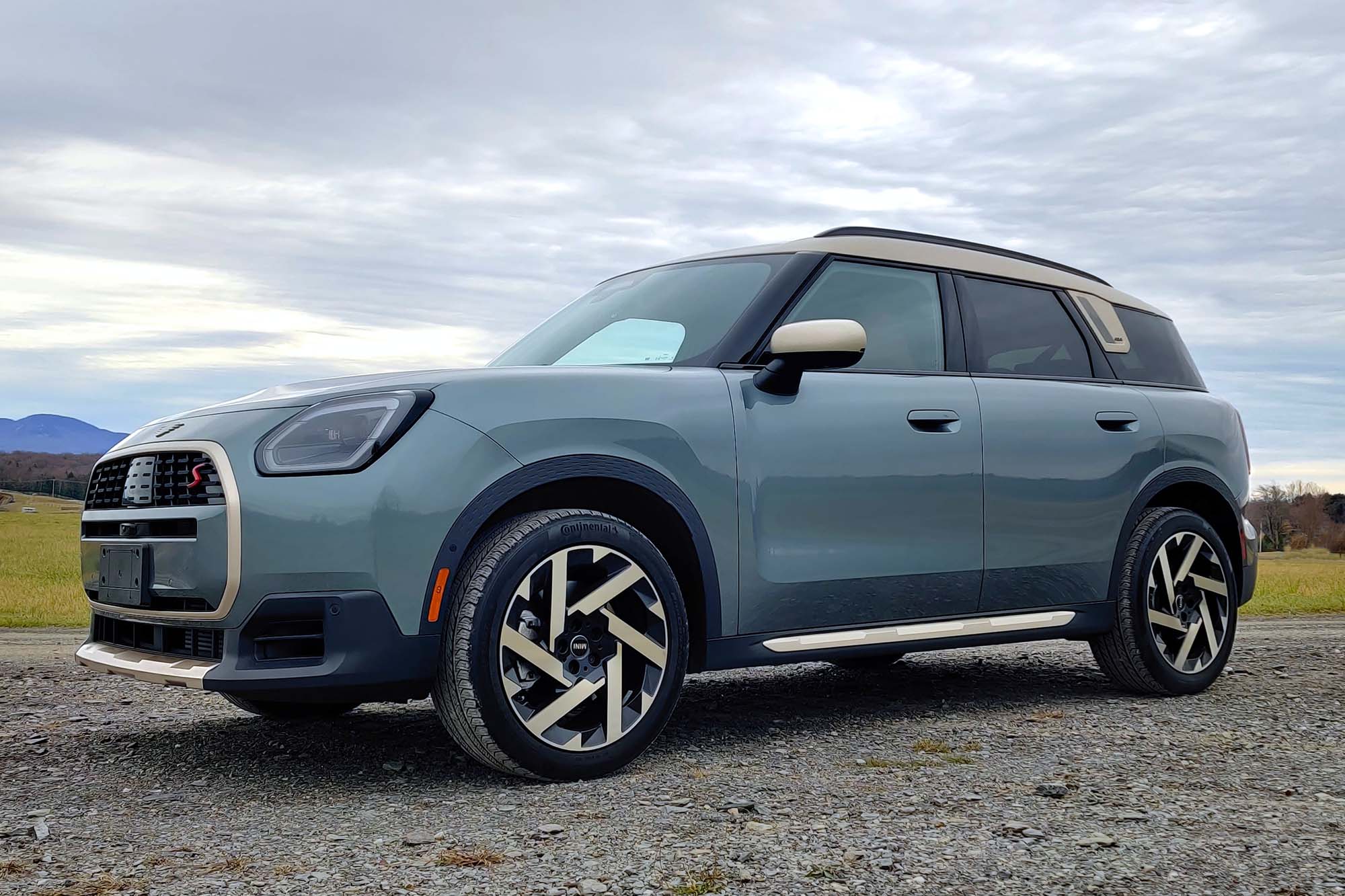 2025 Mini Countryman S All4 in Smokey Green with a field, mountains, and gray skies in the background.