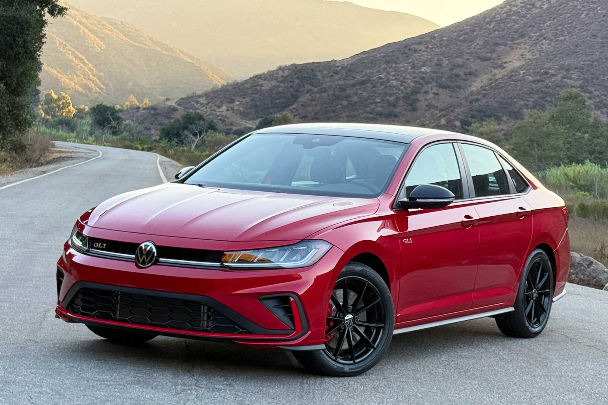 2025 Volkswagen Jetta GLI in Kings Red Metallic with Black package, shown with a road and mountains in the background.