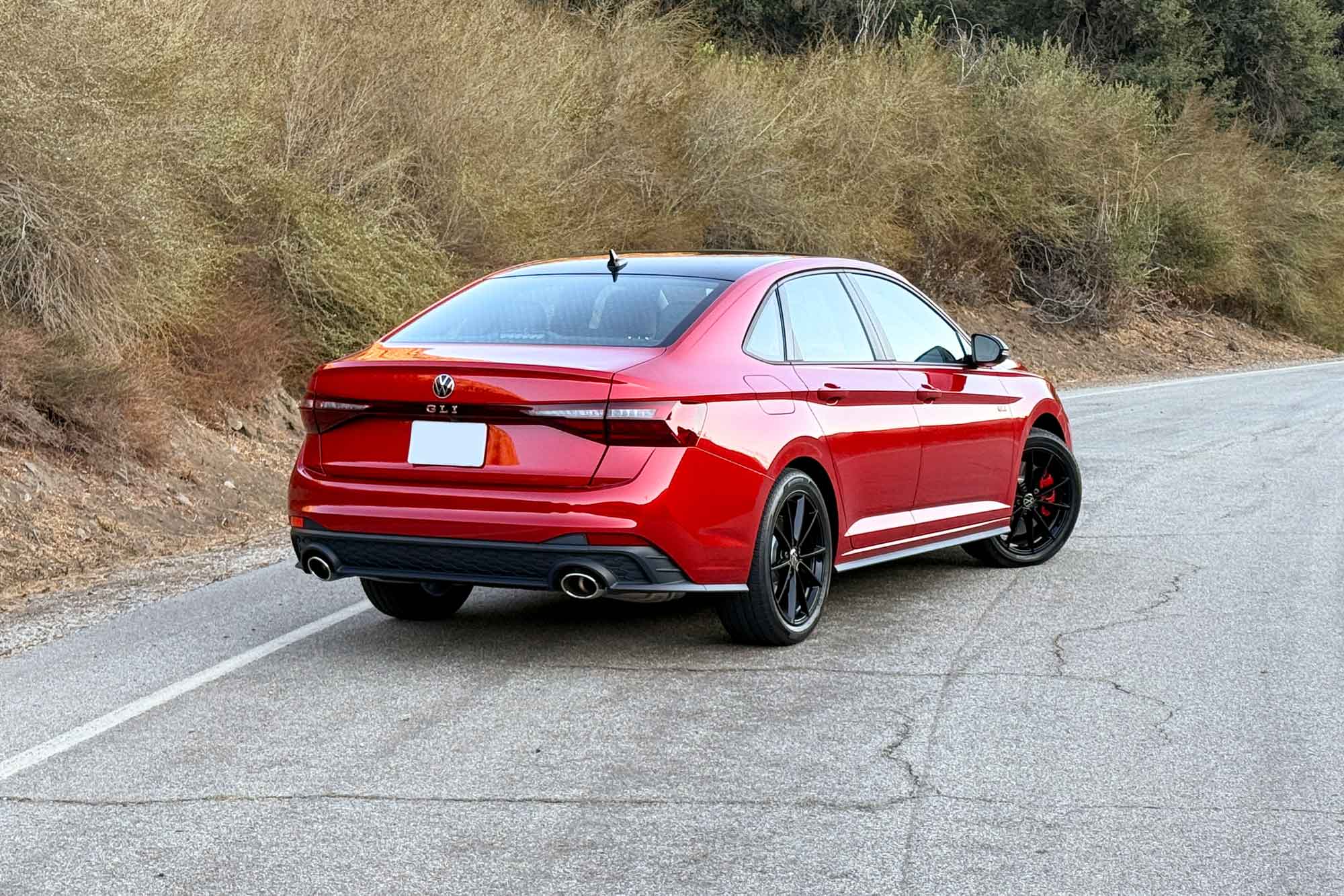 2025 Volkswagen Jetta GLI in Kings Red Metallic with Black package, shown with a brush-covered hillside in the background.