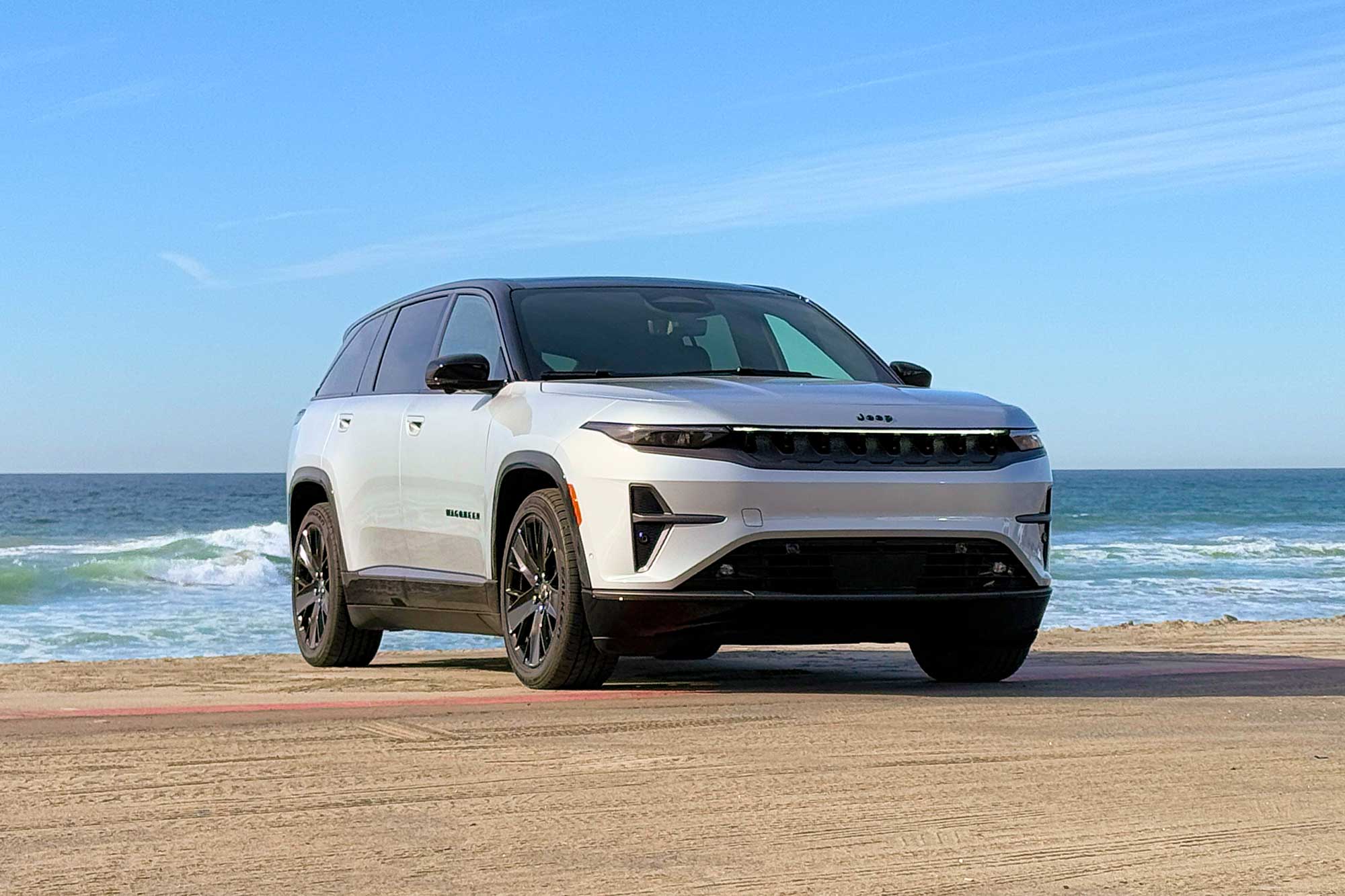 2024 Jeep Wagoneer S Launch Edition in Silver Zynith parked at a beach with the ocean and blue sky in the background.