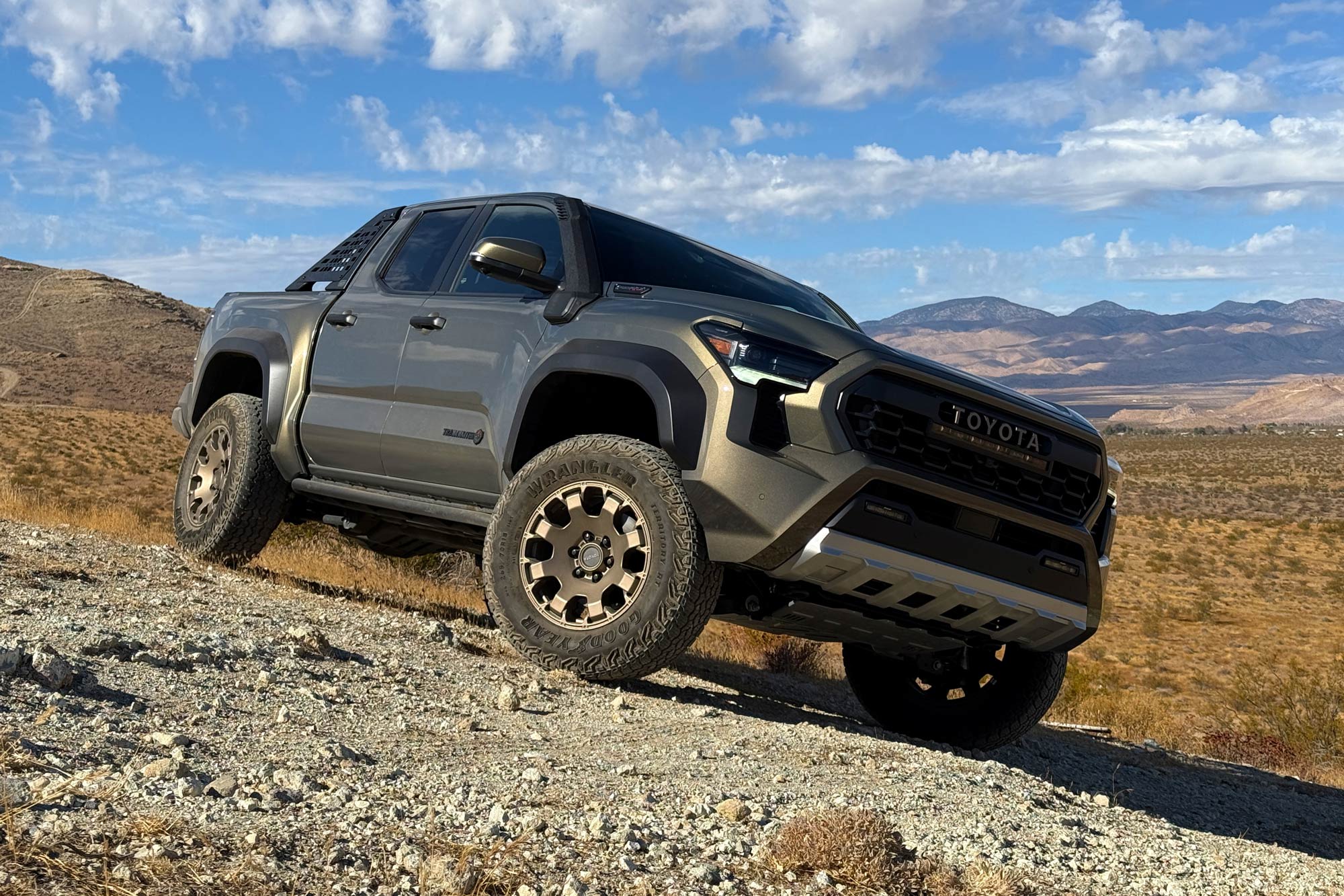 Front quarter 2024 Toyota Tacoma Trailhunter in Bronze Oxide with the desert, mountains, and cloudy blue skies in the background