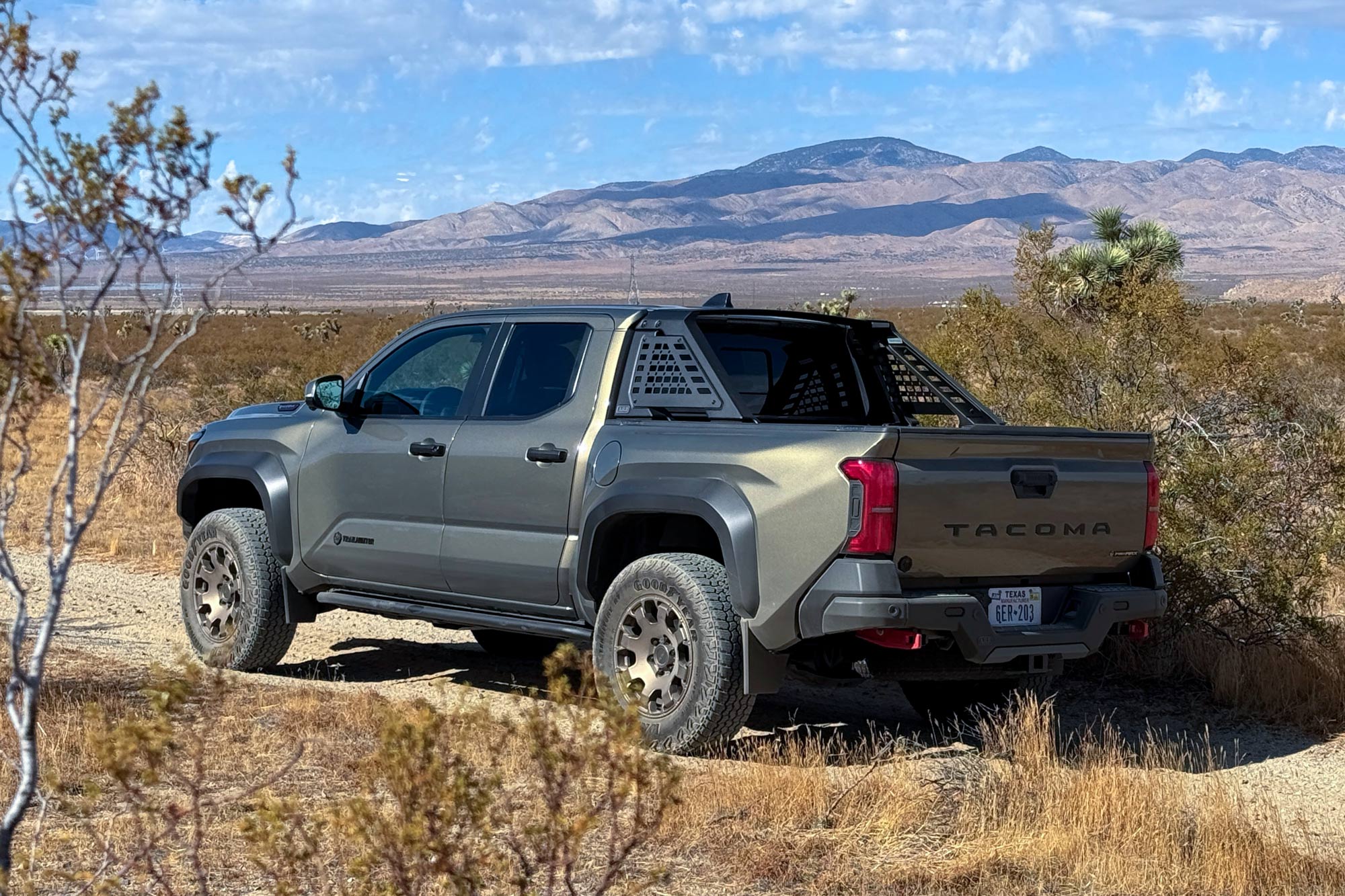 Rear quarter 2024 Toyota Tacoma Trailhunter in Bronze Oxide with the desert, mountains, and cloudy blue skies in the background