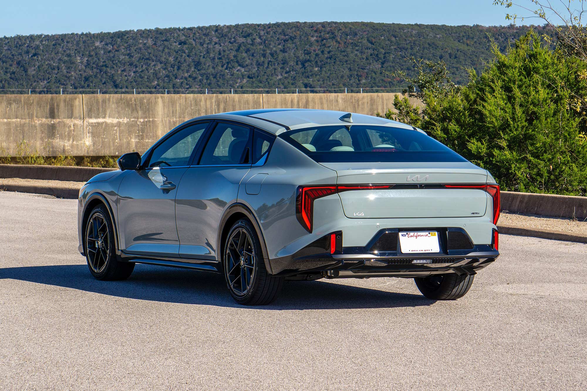 2025 Kia K4 GT-Line Turbo in Morning Haze with a concrete wall, trees, and blue sky in the background