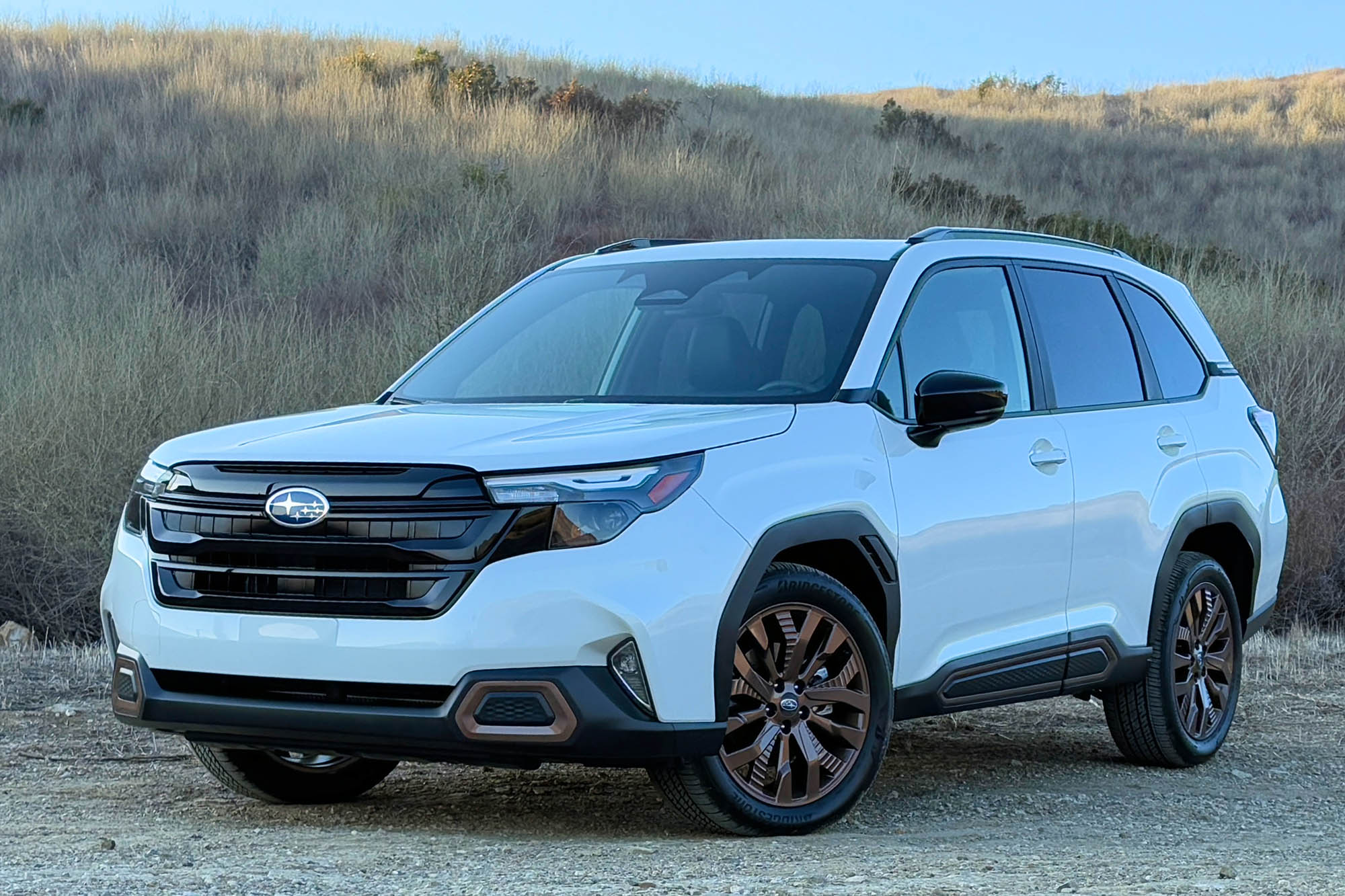 2025 Subaru Forester Sport in Crystal White Pearl with a brush-covered hillside in the background.