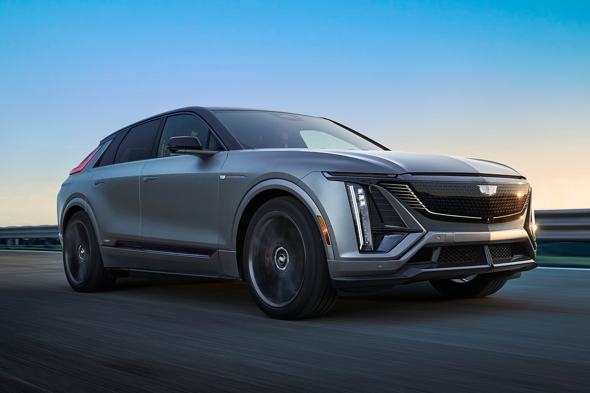 Front-right view of a silver 2025 Cadillac Lyriq-V driving on a highway.