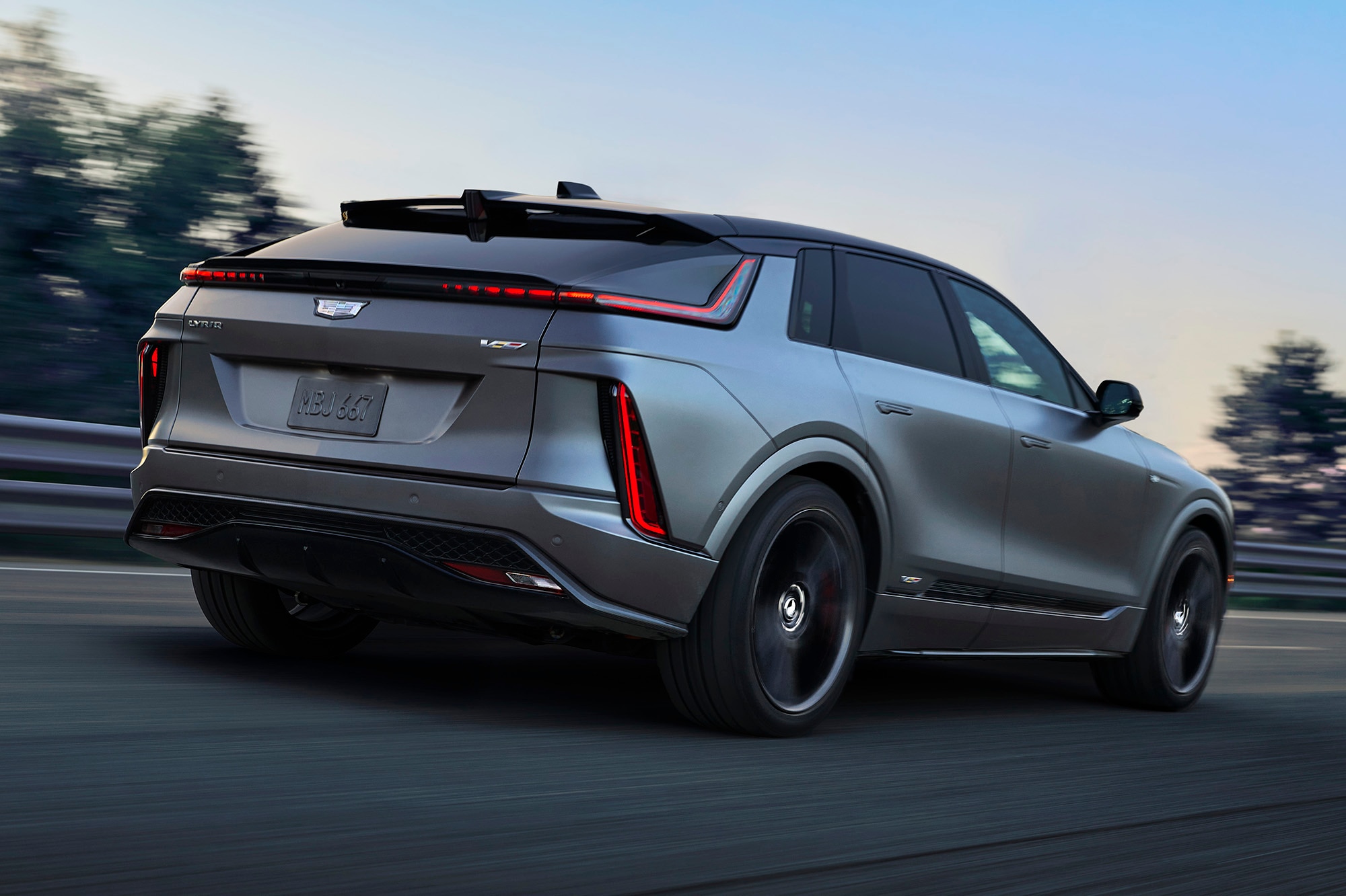 Rear-right view of a silver 2025 Cadillac Lyriq-V driving on a highway.