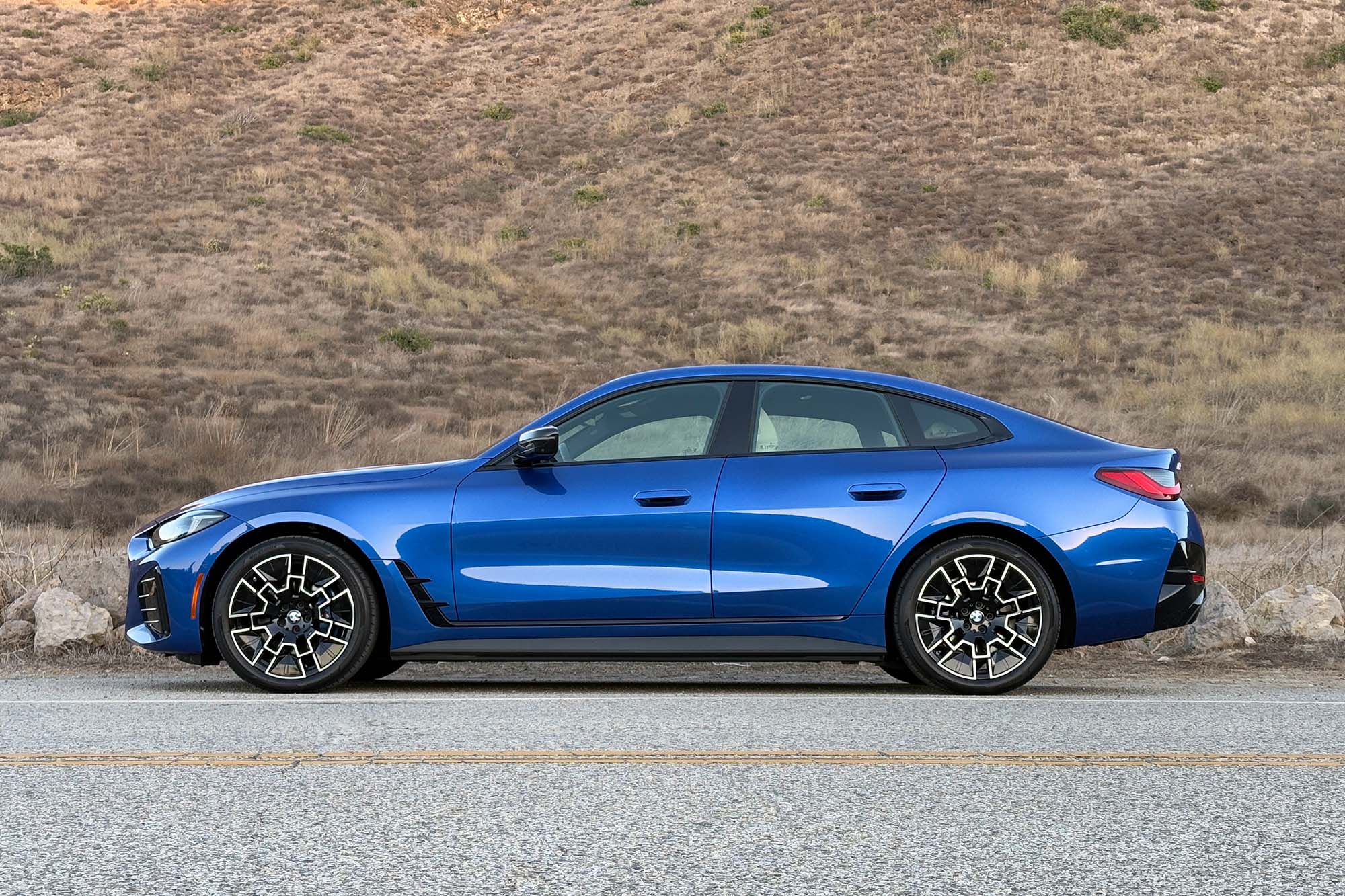 2025 BMW i4 eDrive40 in Portimao Blue with a mountainside in the background.